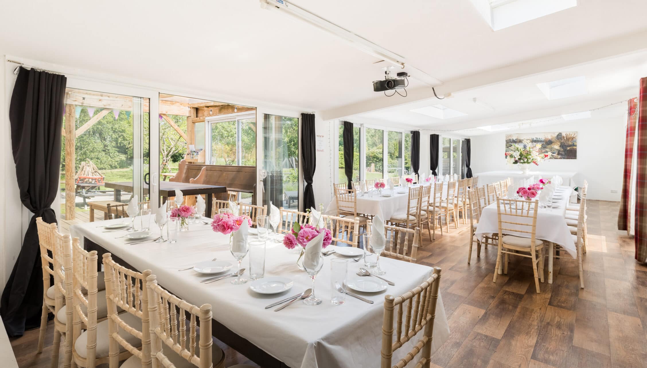 Upper Court, Gloucestershire – Bright event space with white-clothed dining tables, pink floral centrepieces and garden views.