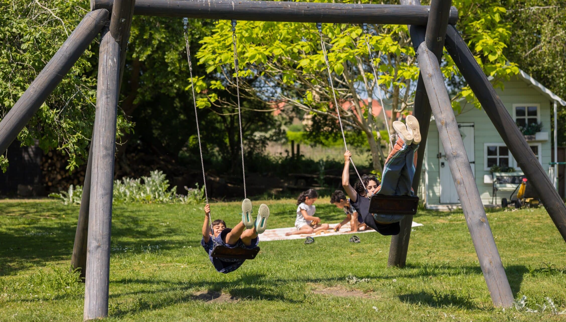 Upper Court, Gloucestershire – Children playing on wooden swing frame in sunny garden with country house in background.