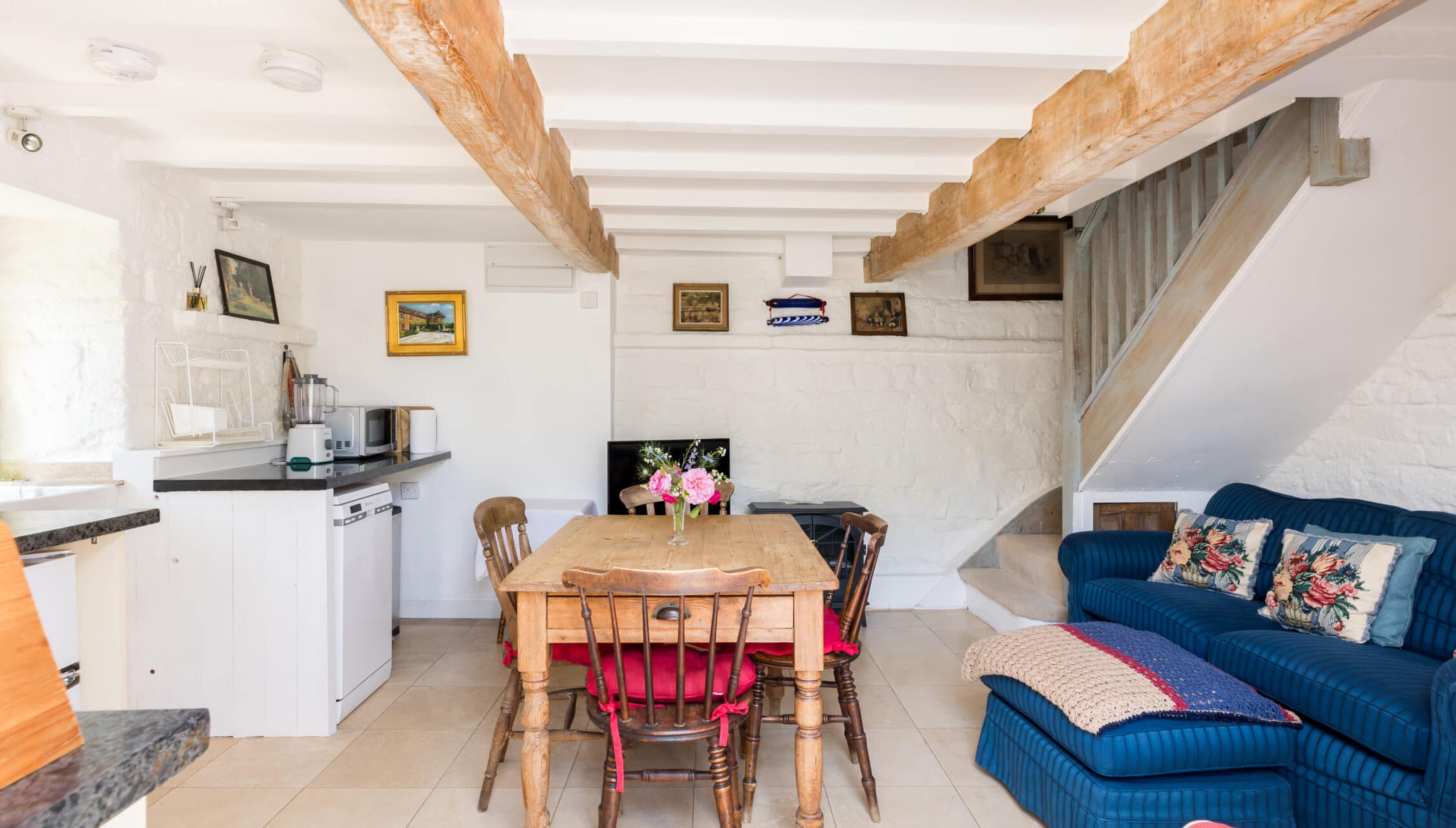 Upper Court, Gloucestershire – Open-plan living space with exposed wooden beams, wooden dining table, and blue upholstered sofa.