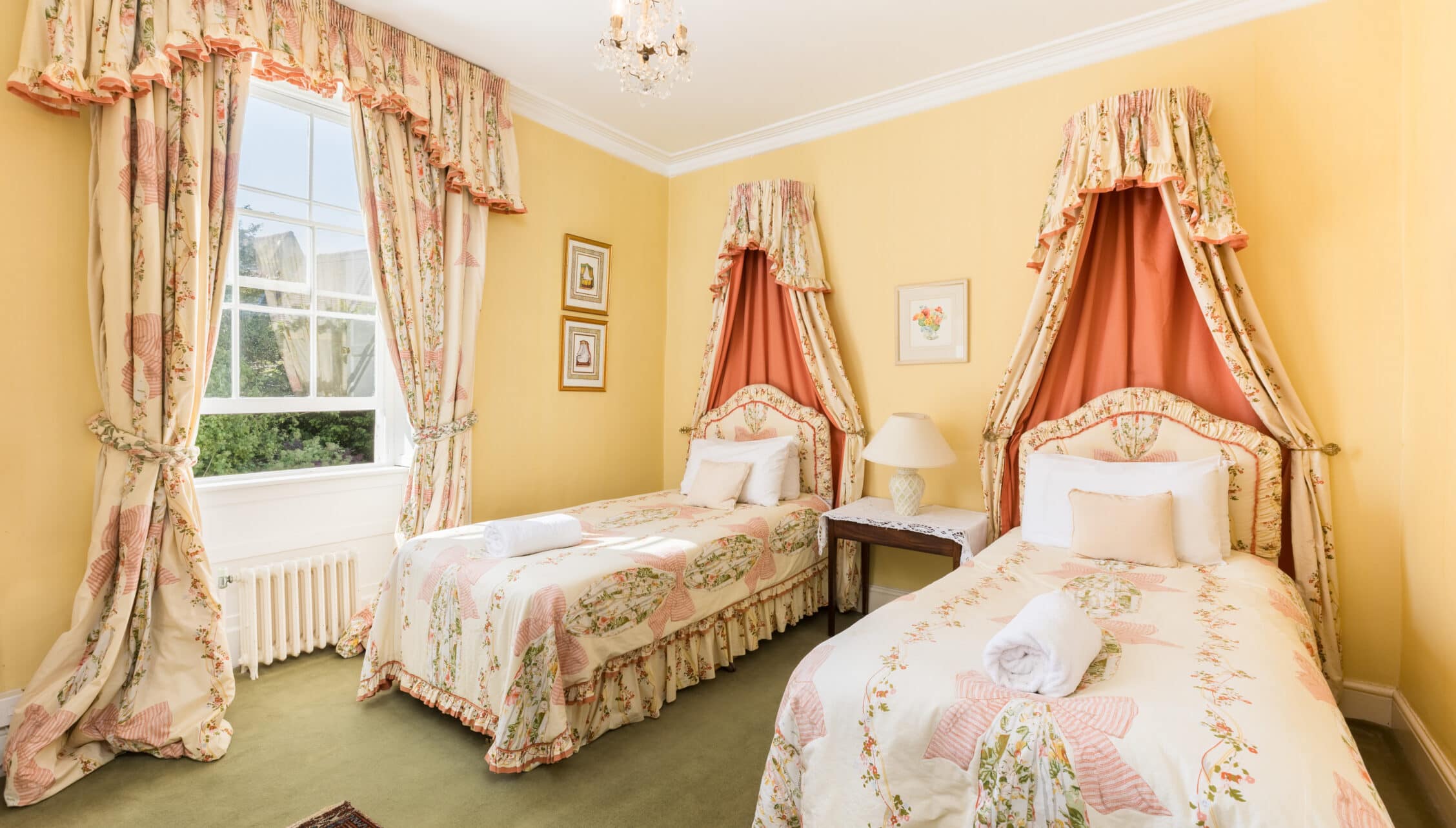Upper Court, Gloucestershire – Twin four-poster beds with fabric canopies in yellow bedroom with floral curtains.