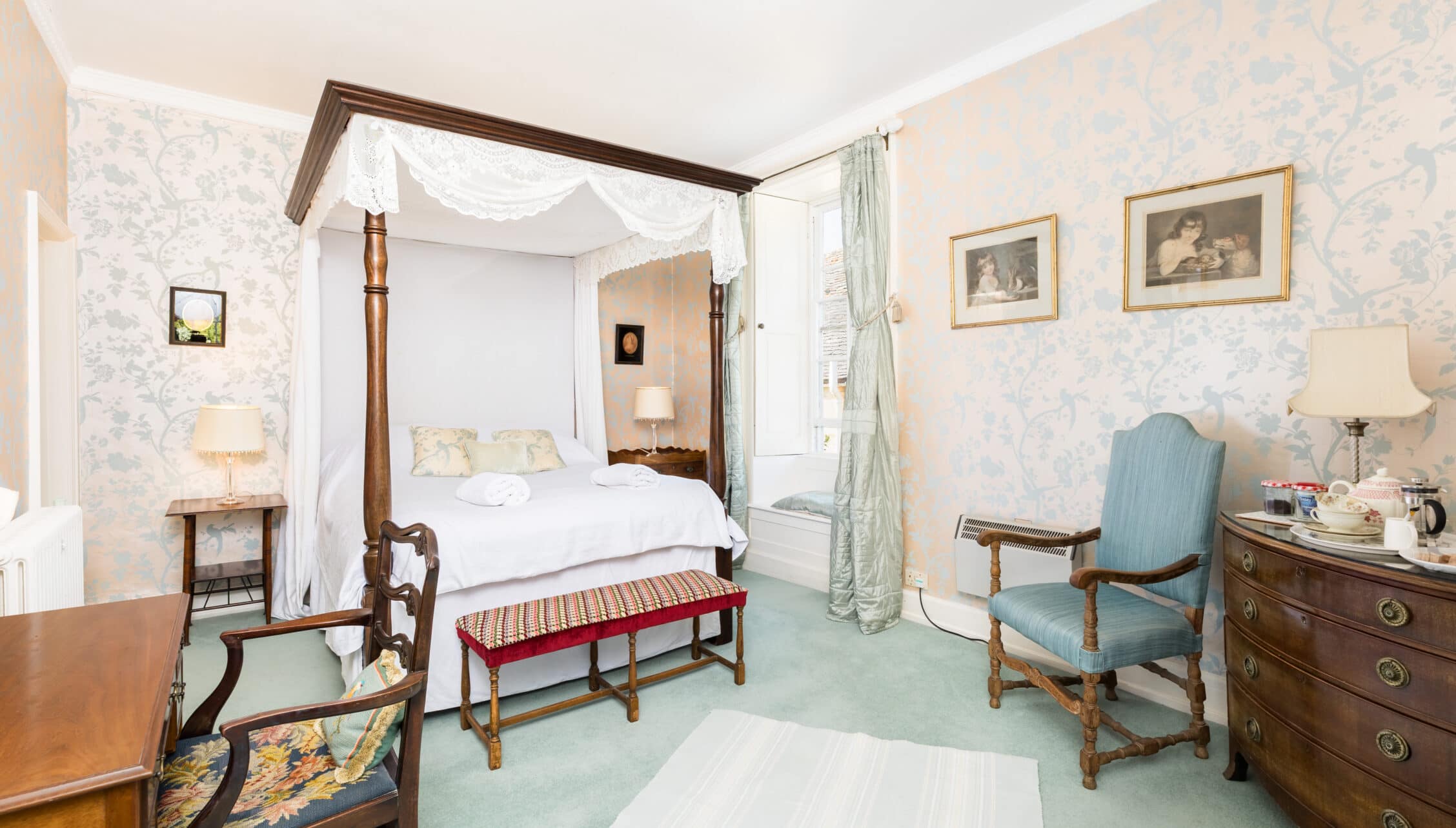 Upper Court, Gloucestershire – Four-poster bed with white drapes in period bedroom with blue upholstered chair.
