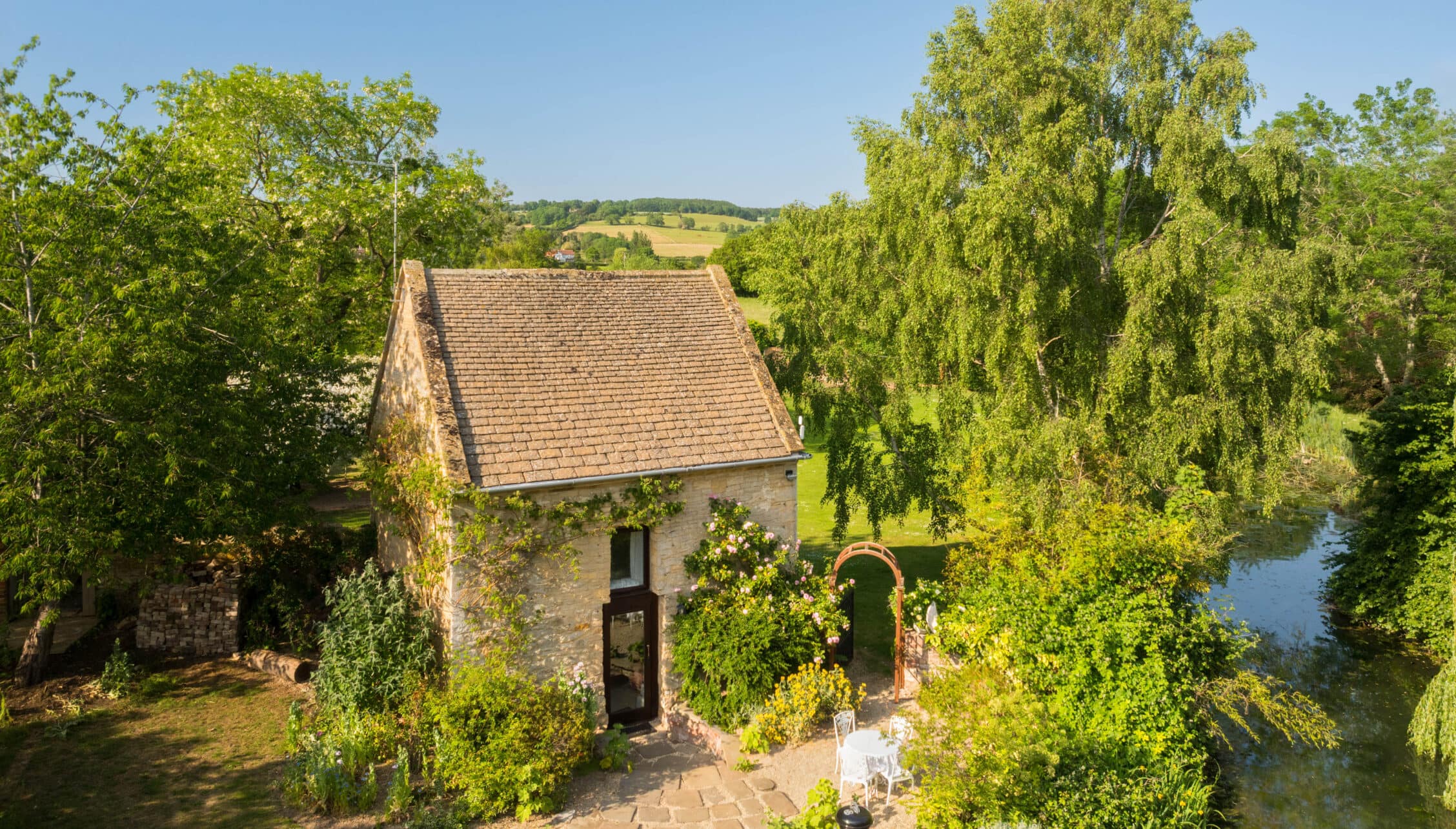 Upper Court, Gloucestershire – Stone cottage with ivy-covered walls beside river and weeping willow trees.
