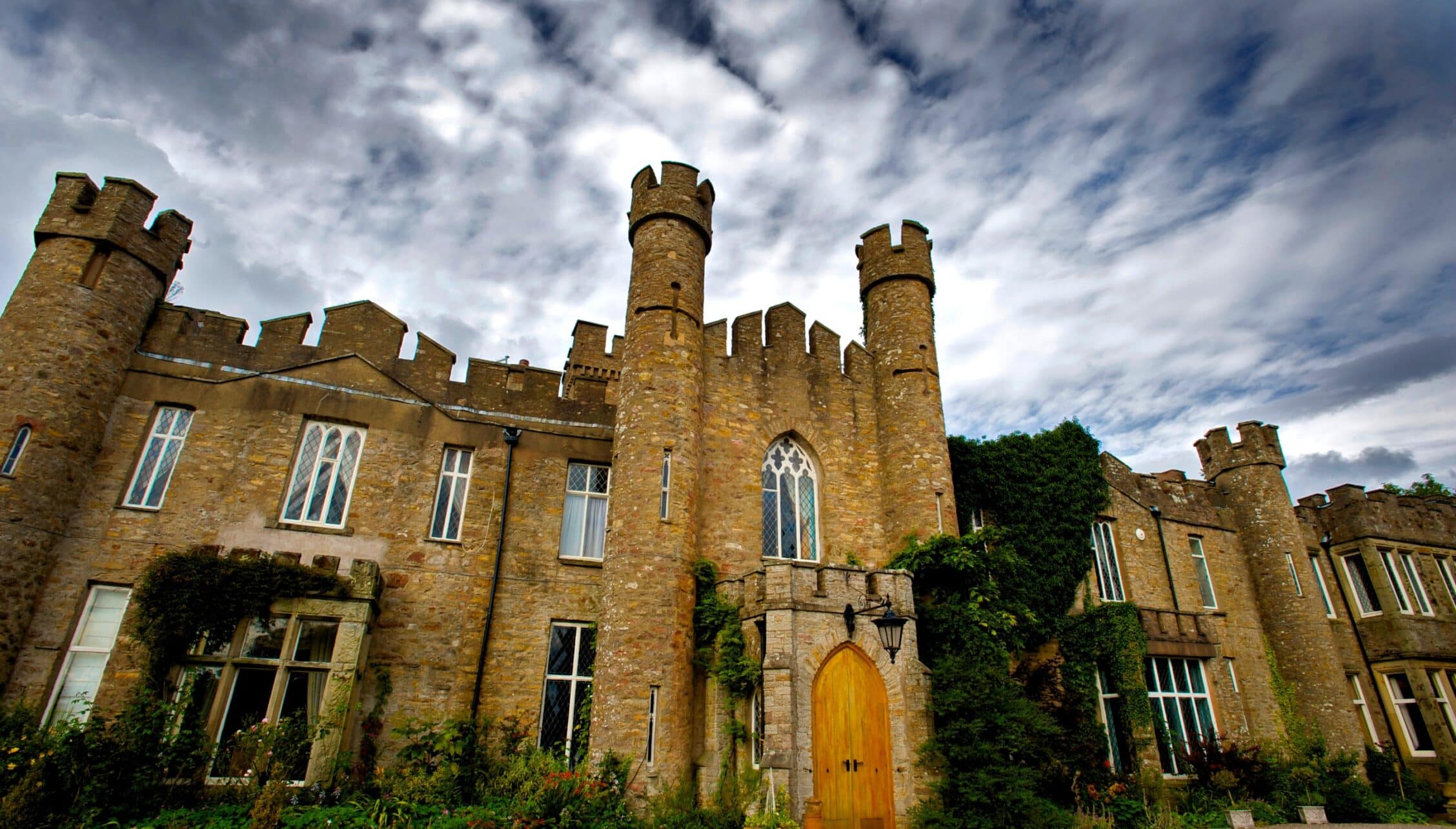 Augill Castle, Cumbria – Stone castle with castellated towers, ivy-clad walls and Gothic yellow door.