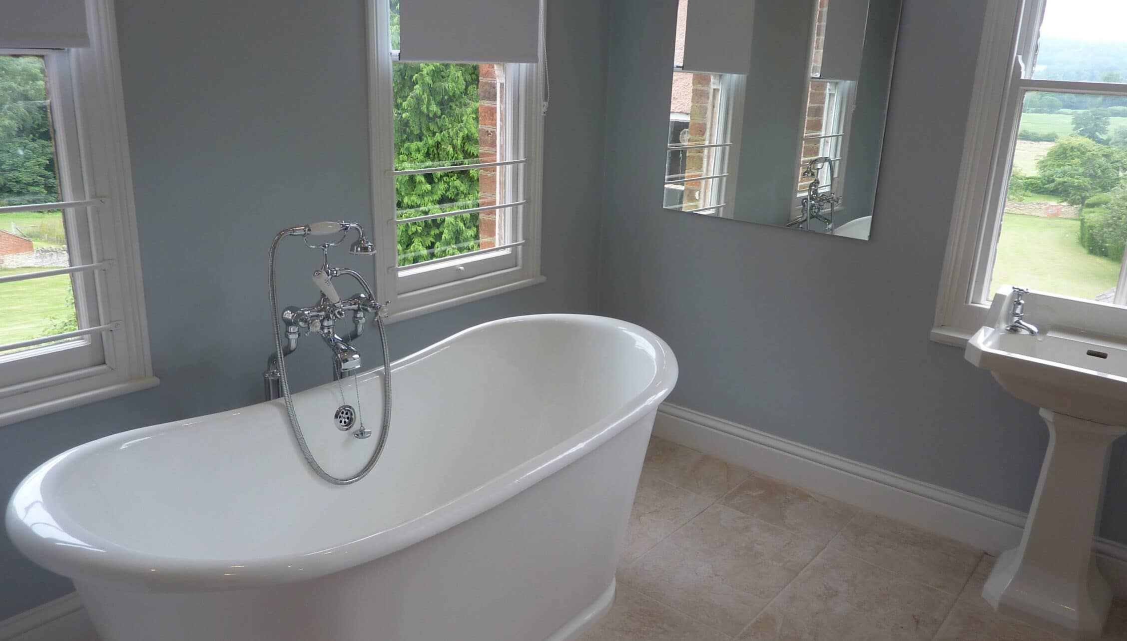 Barton Court, Herefordshire – Bathroom with freestanding bath, pedestal sink, and countryside views through windows.