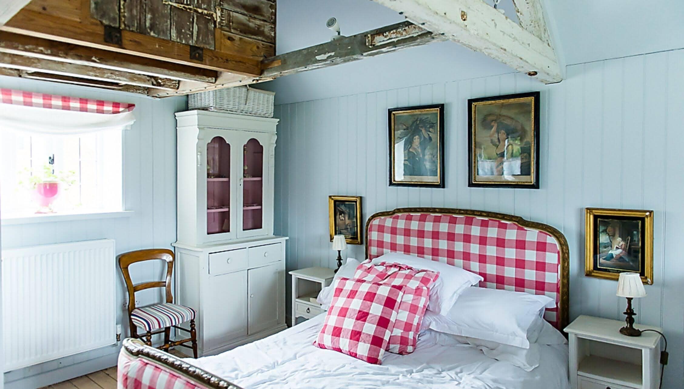 Barton Court, Herefordshire – Bedroom with pink gingham headboard, white wood panelling, and period portraits.