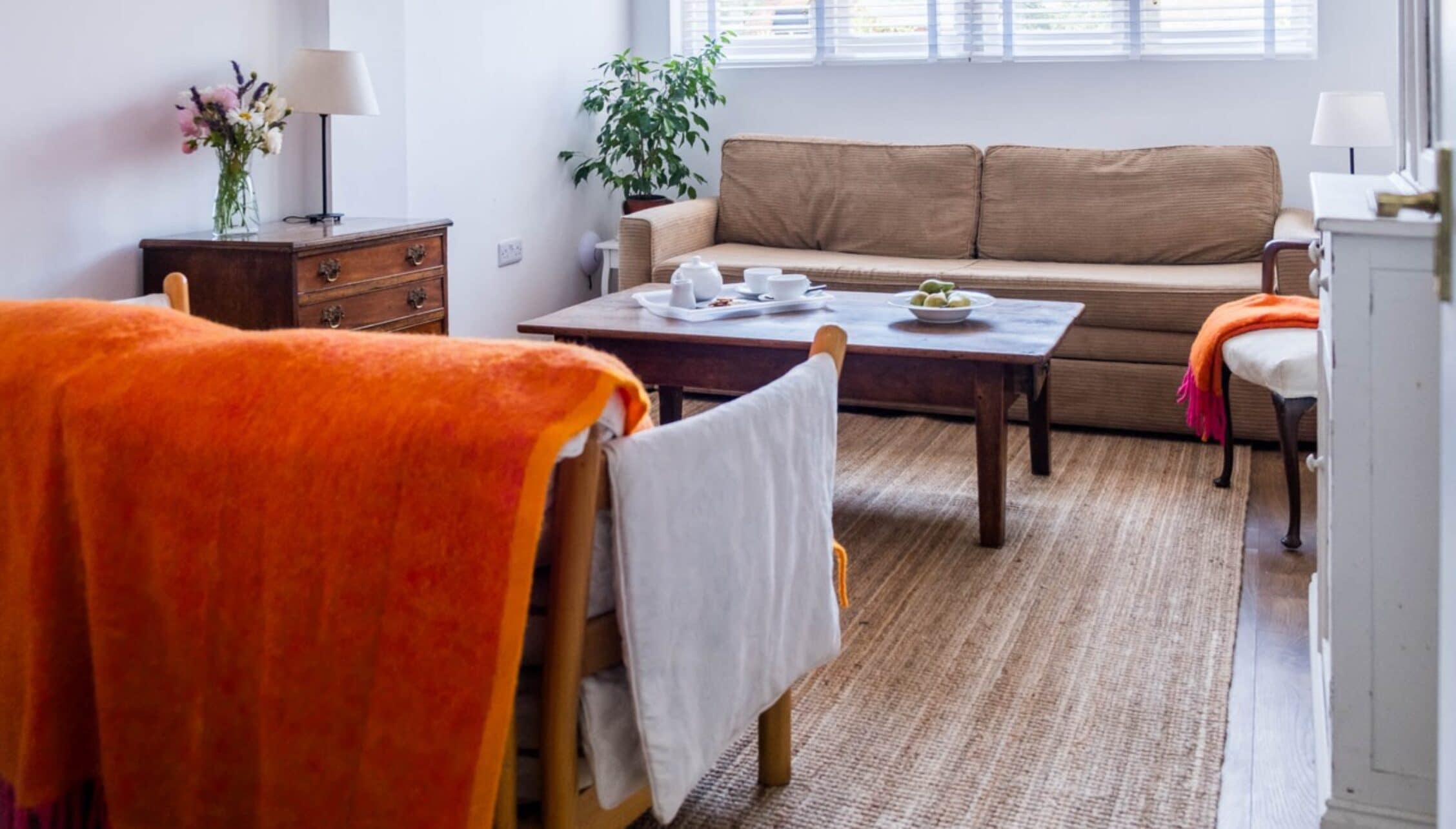 Barton Court, Herefordshire – Bright sitting room with beige sofa, wooden furniture and orange throw blanket.