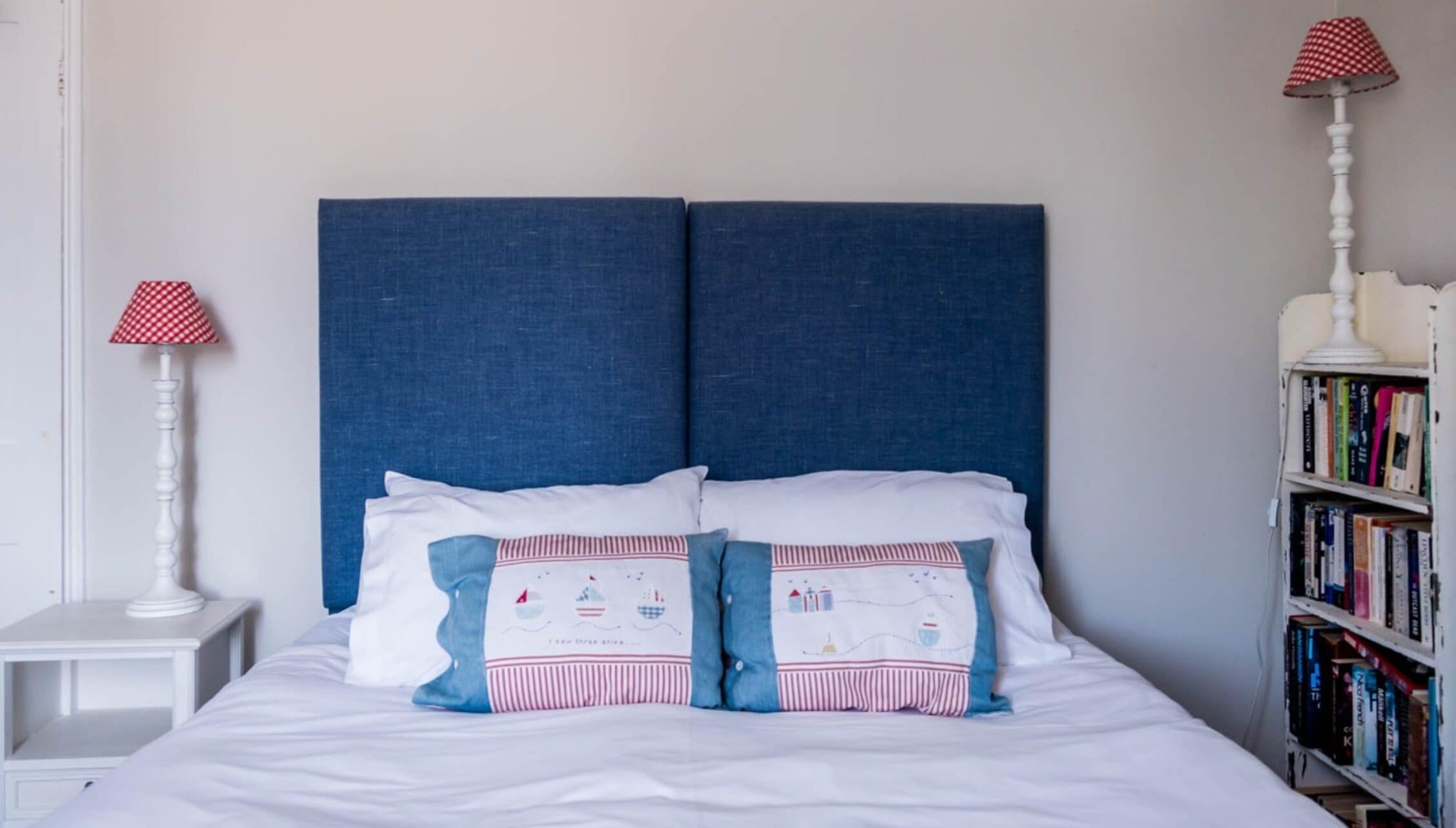 Barton Court, Herefordshire – Bedroom with blue upholstered headboard, white bedding, and bookshelf storage unit.