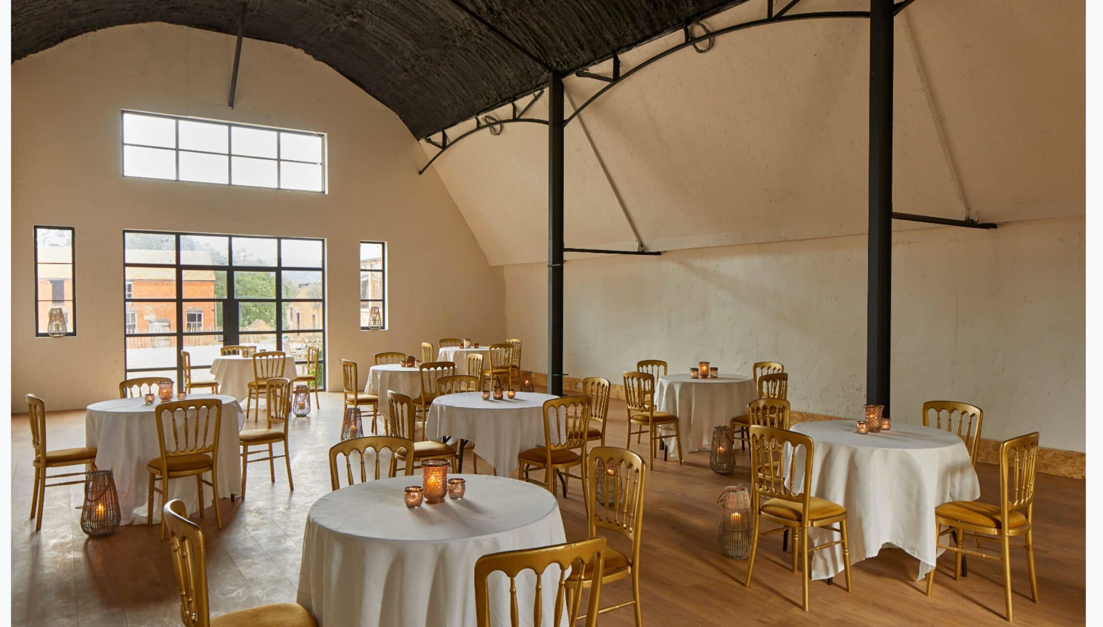 Barton Court, Herefordshire – Converted barn event space with round tables, wooden chairs and industrial ceiling beams.
