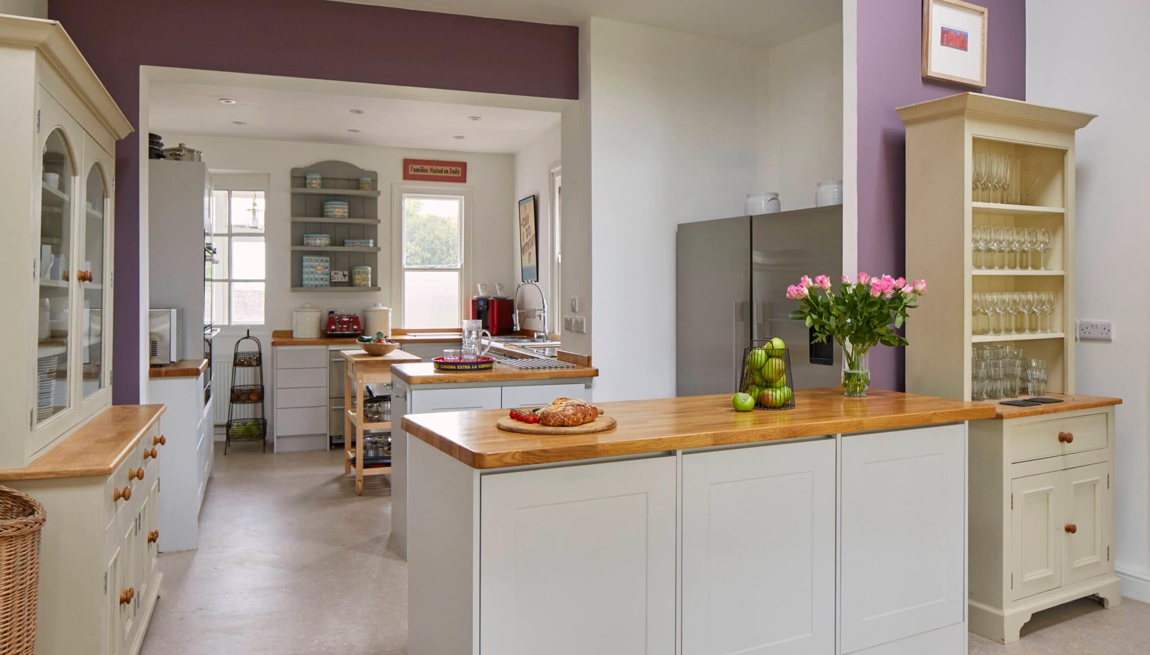 Barton Court, Herefordshire – Modern kitchen with cream cabinetry, wooden worktops, and purple accent walls.