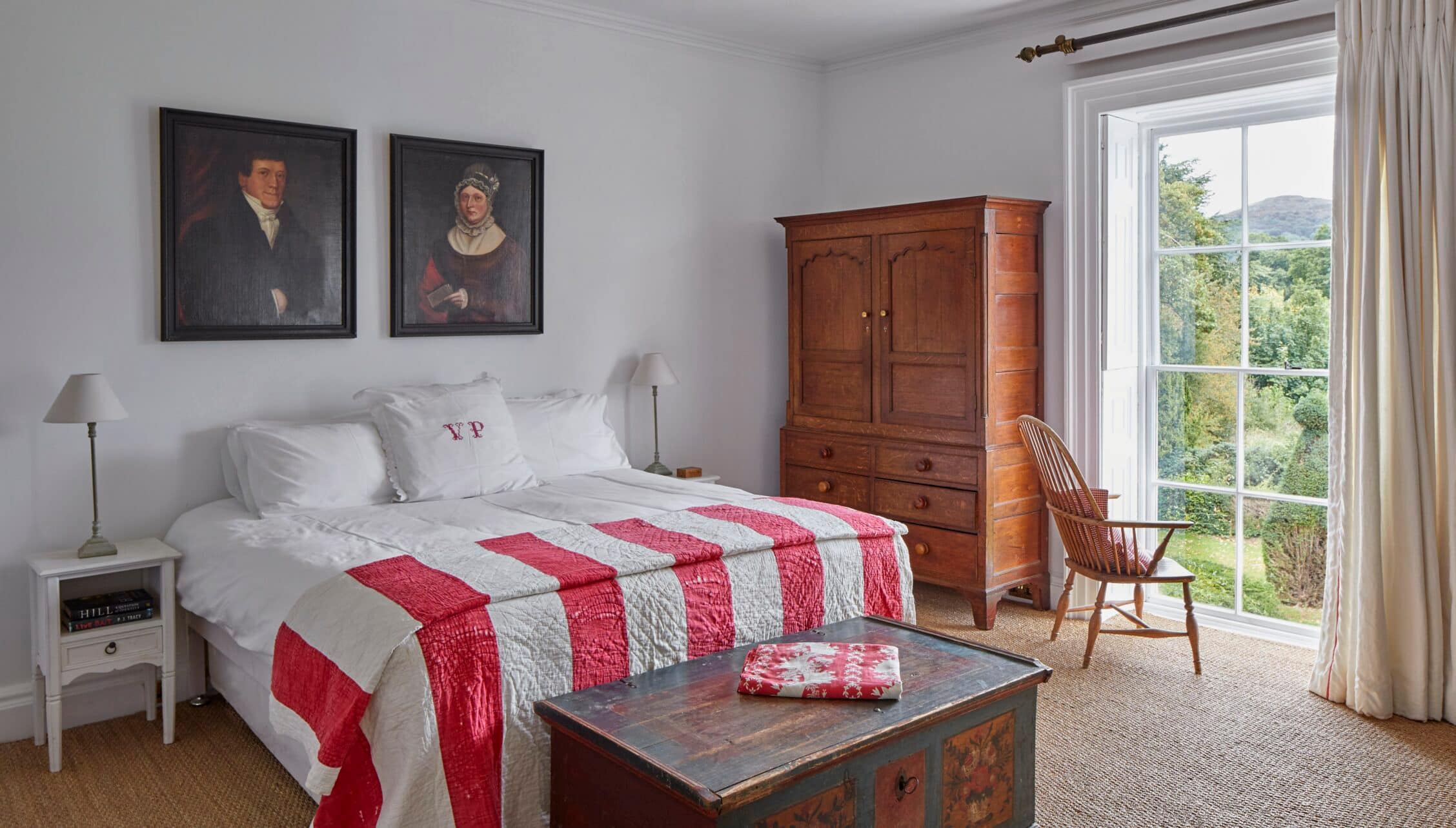 Barton Court, Herefordshire – Bedroom with red and white quilt, wooden wardrobe, and French doors opening to countryside views.