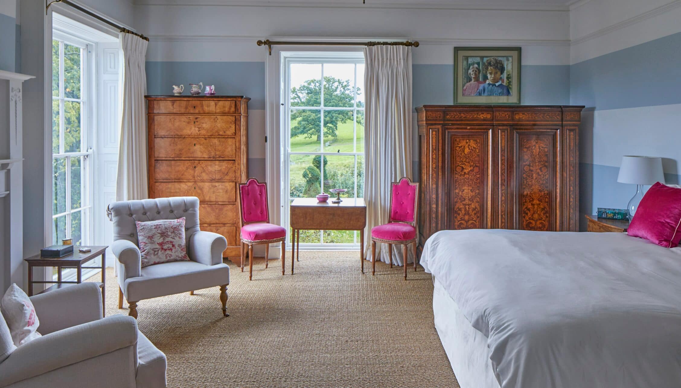 Barton Court, Herefordshire – Spacious bedroom with blue walls, antique wooden furniture and countryside views through large windows.