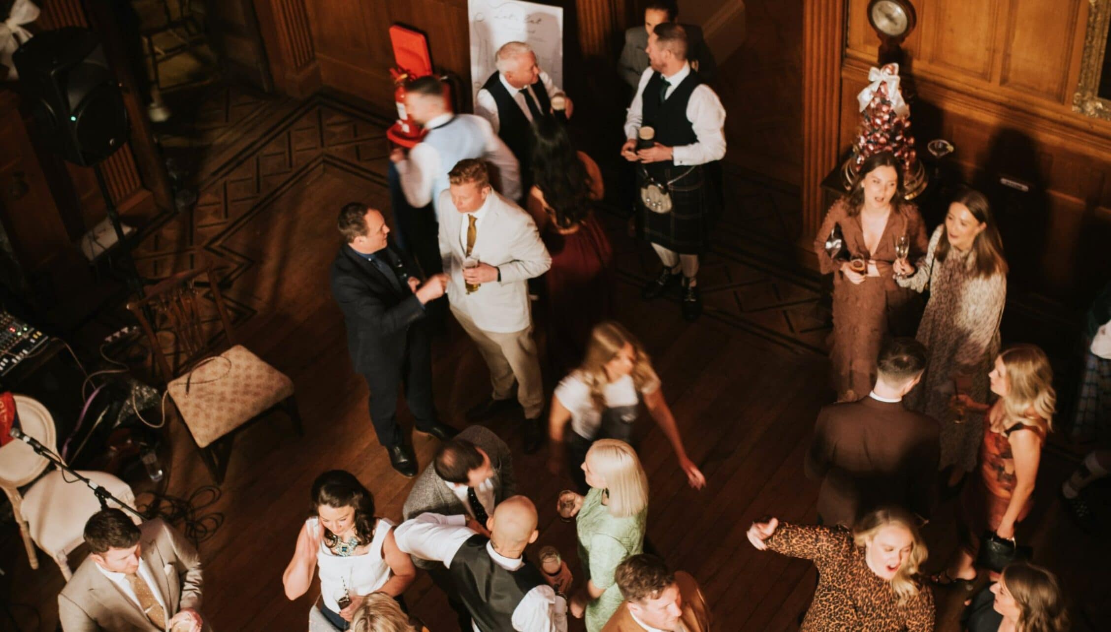 Berwick House, Shropshire – Overhead view of guests dancing and socialising in wood-panelled hall with geometric floor.