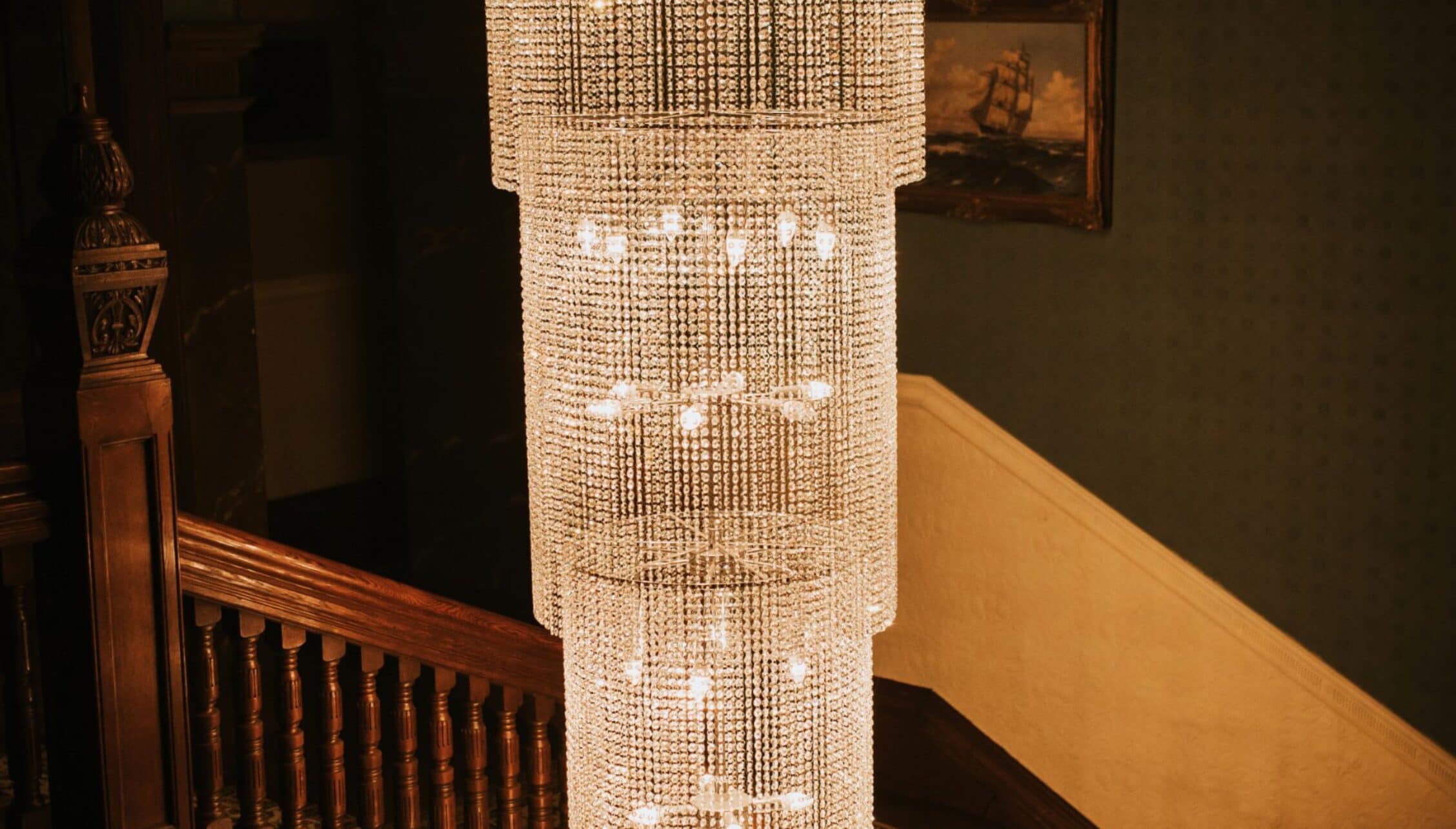 Berwick House, Shropshire – Crystal chandelier with cylindrical shade suspended above wooden staircase.