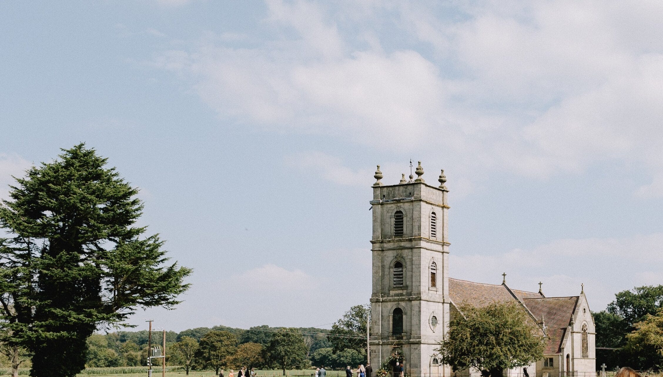 Berwick House, Shropshire – Stone church tower with decorative pinnacles beside mature lime tree and countryside grounds.