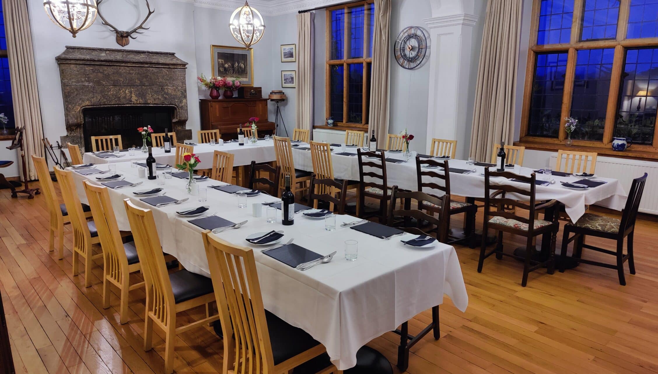 Bossington Hall, Somerset – Formal dining room with stone fireplace, white-clothed tables and wooden chairs.