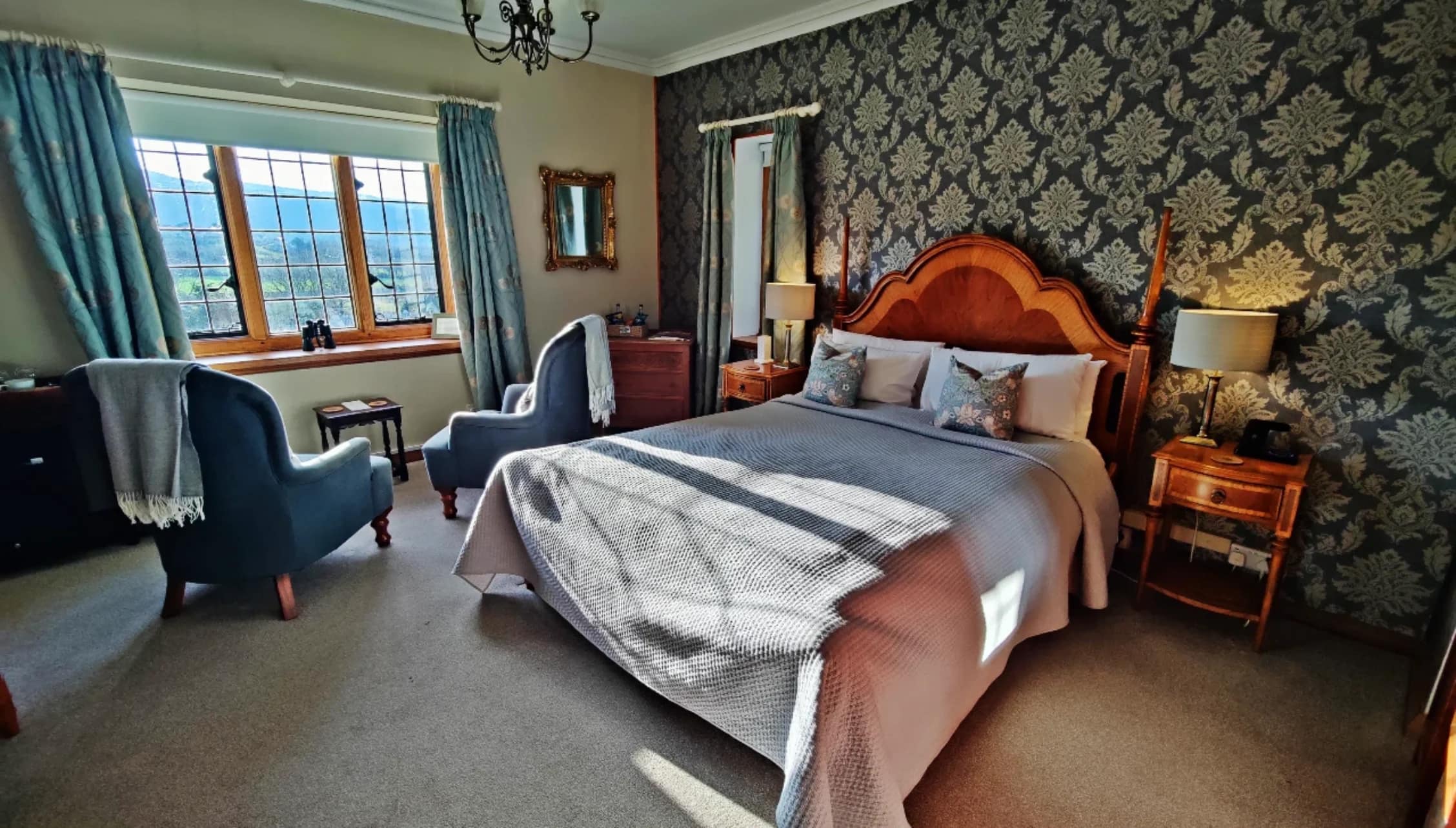 Bossington Hall, Somerset – Master bedroom with four-poster bed, damask wallpaper and bay windows overlooking countryside.