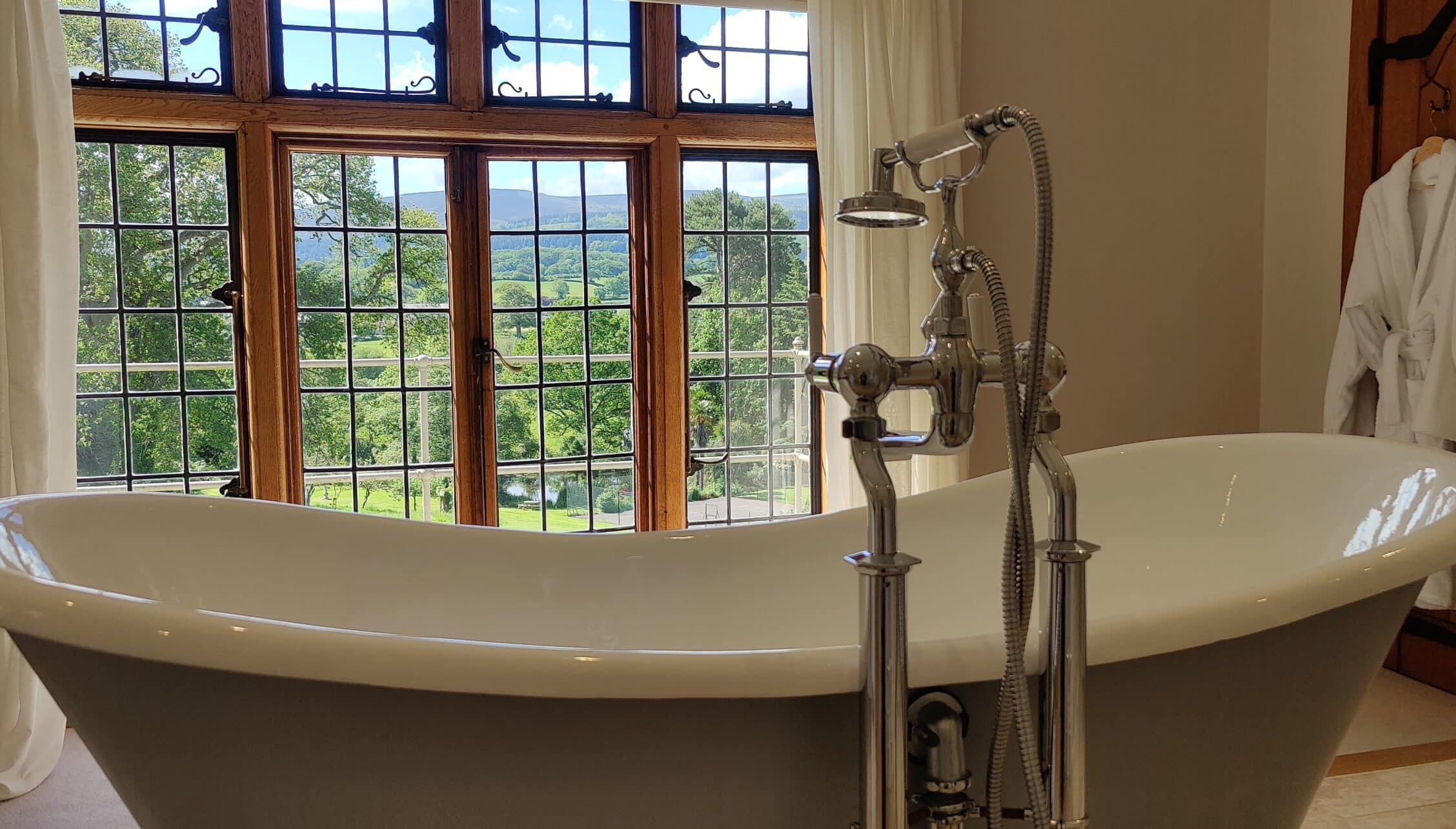 Bossington Hall, Somerset – Freestanding bath with chrome taps and large multi-pane windows overlooking countryside.