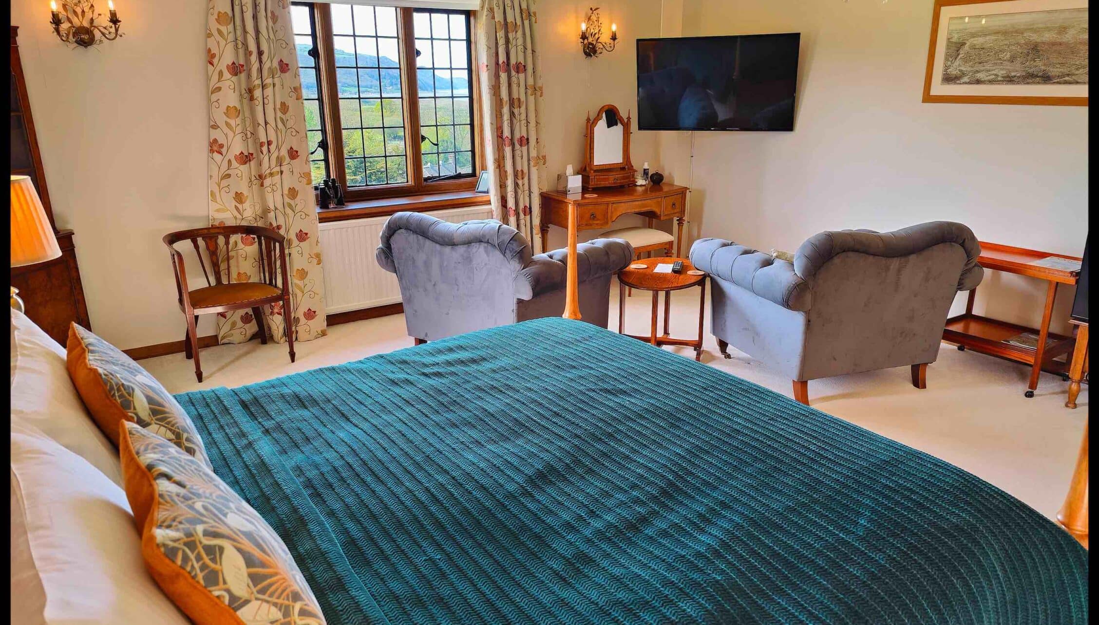 Bossington Hall, Somerset – Spacious bedroom with king bed, upholstered armchairs and countryside views through large windows.
