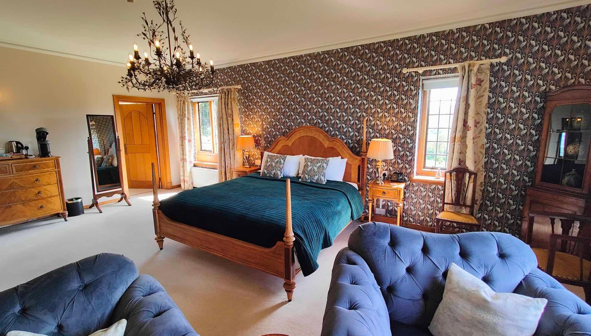 Bossington Hall, Somerset – Spacious bedroom with four-poster bed, patterned wallpaper, and blue velvet seating.