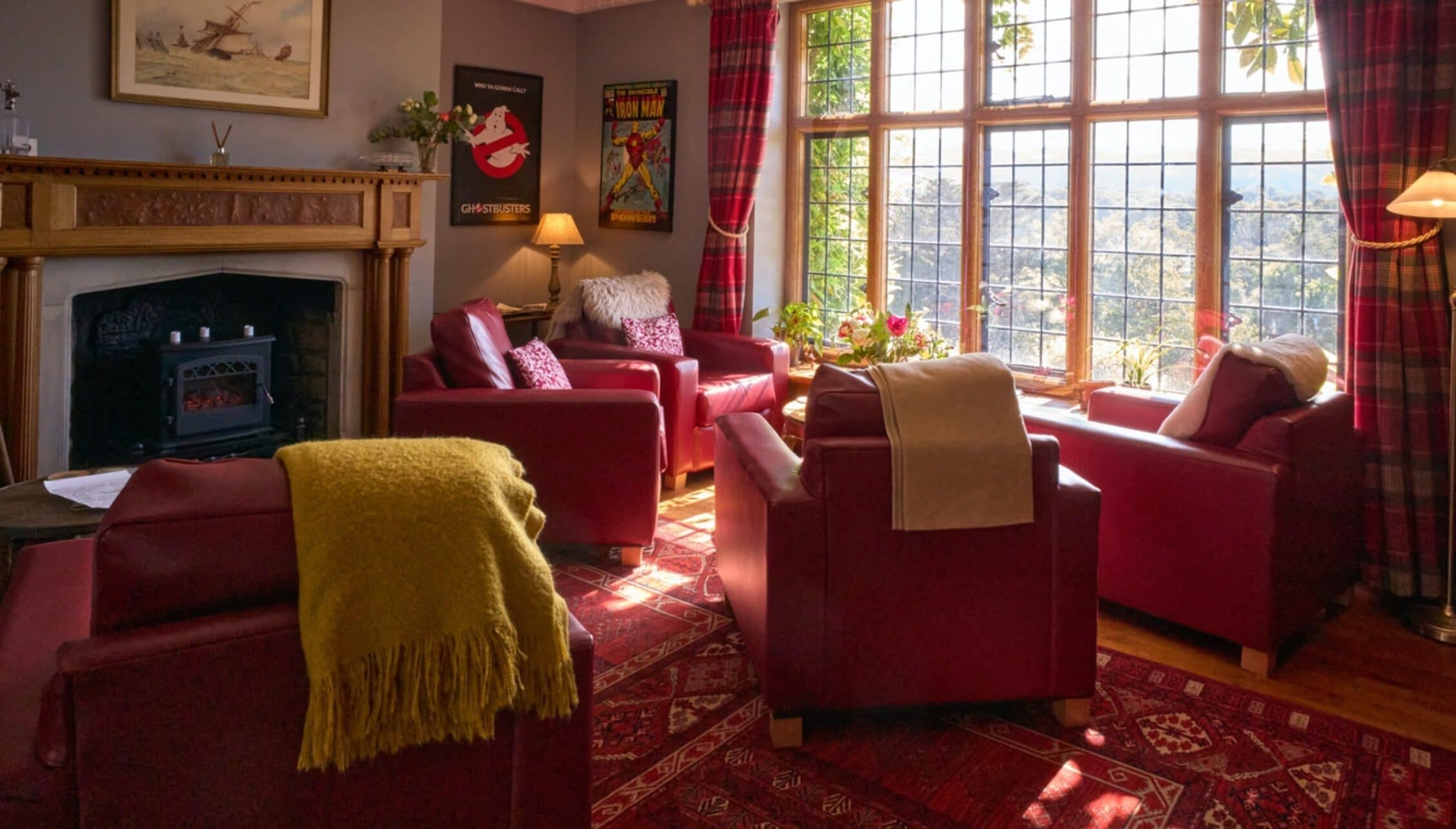 Bossington Hall, Somerset – Sitting room with red upholstered armchairs, wood-burning stove and large sash windows.