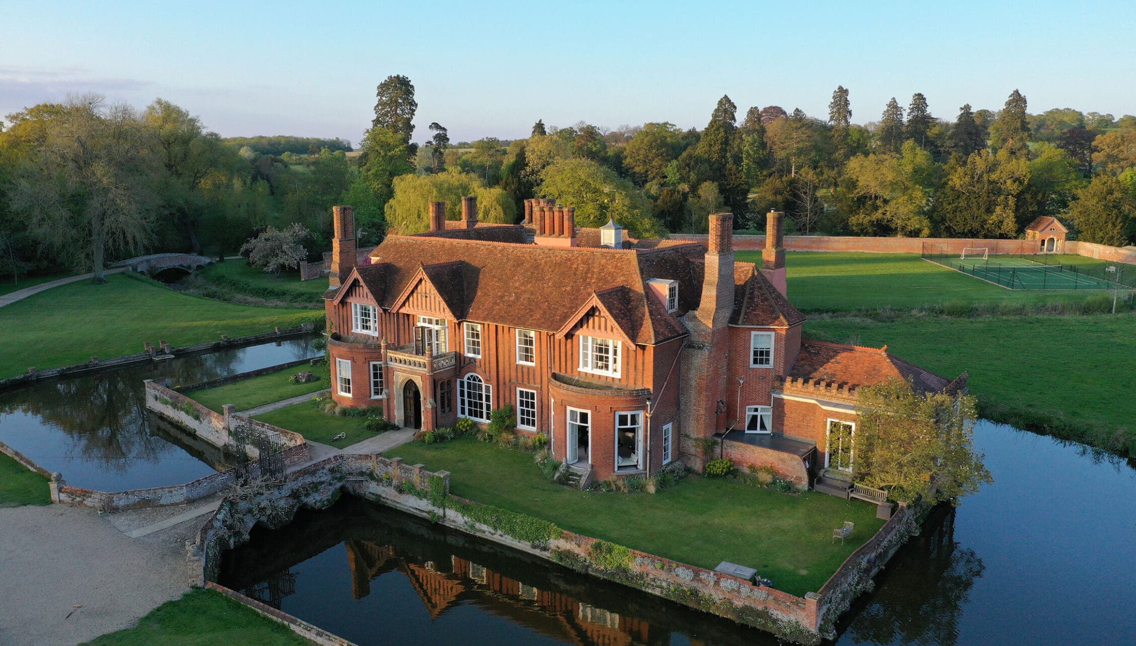 Boxted Hall, Suffolk – Red brick country house with tall chimneys beside moat and bridge.