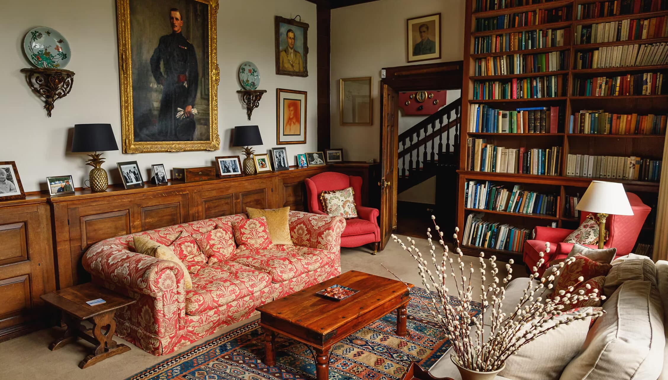 Boxted Hall, Suffolk – Library lounge with red damask sofa, wooden bookshelves, and period portraits.