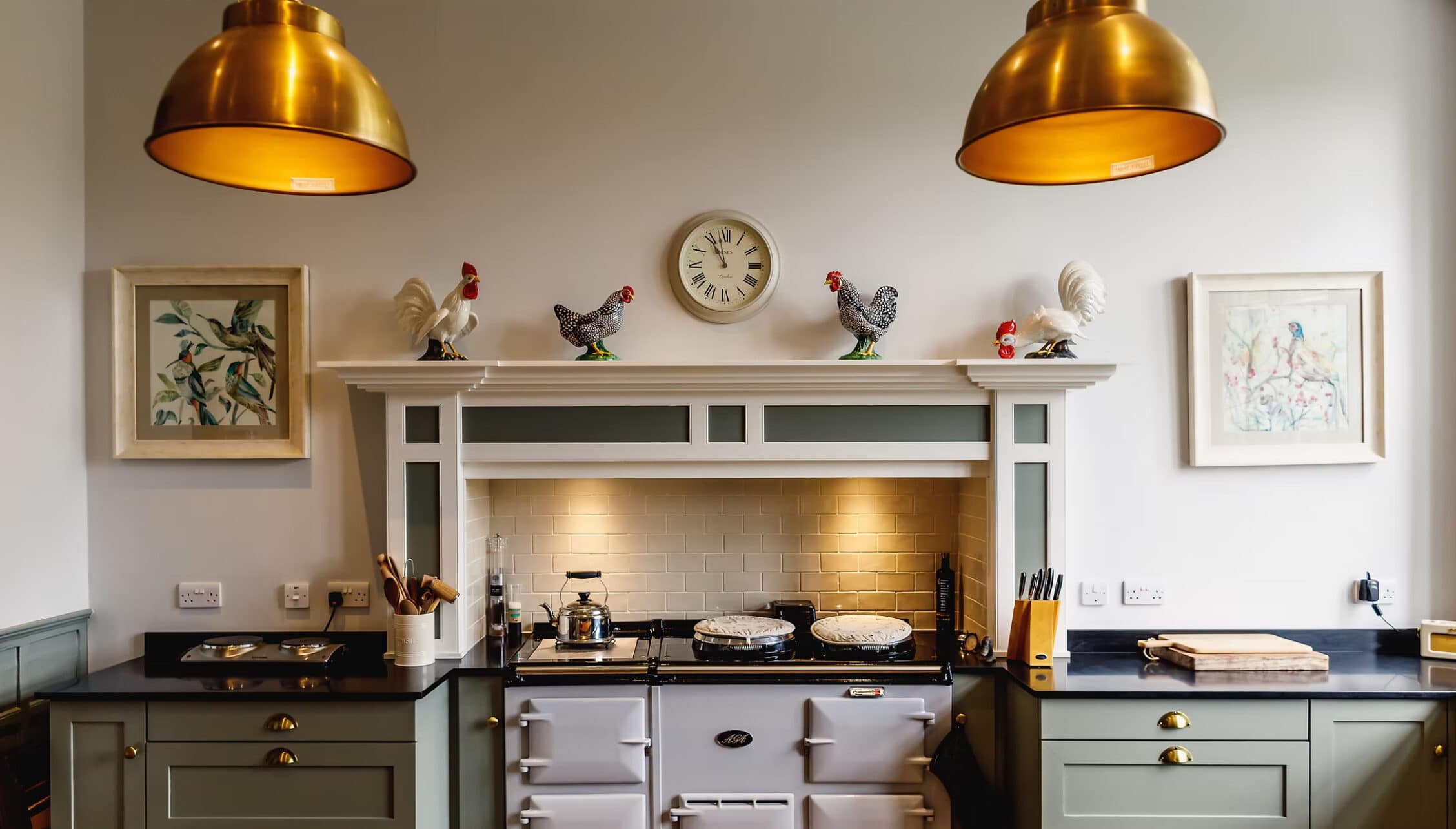 Boxted Hall, Suffolk – Kitchen with cream Aga cooker, brass pendant lights and tiled splashback.