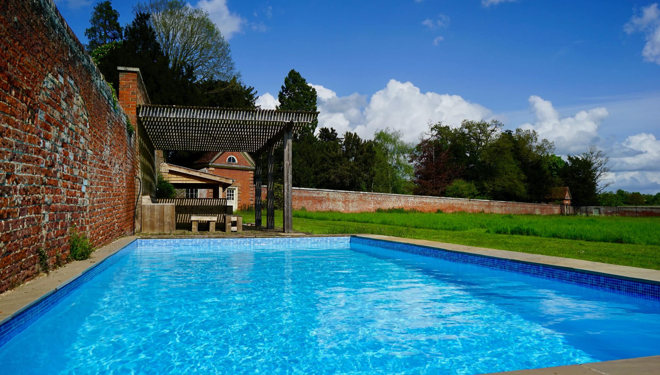 Boxted Hall, Suffolk – Swimming pool with brick wall and pergola beside walled grounds.