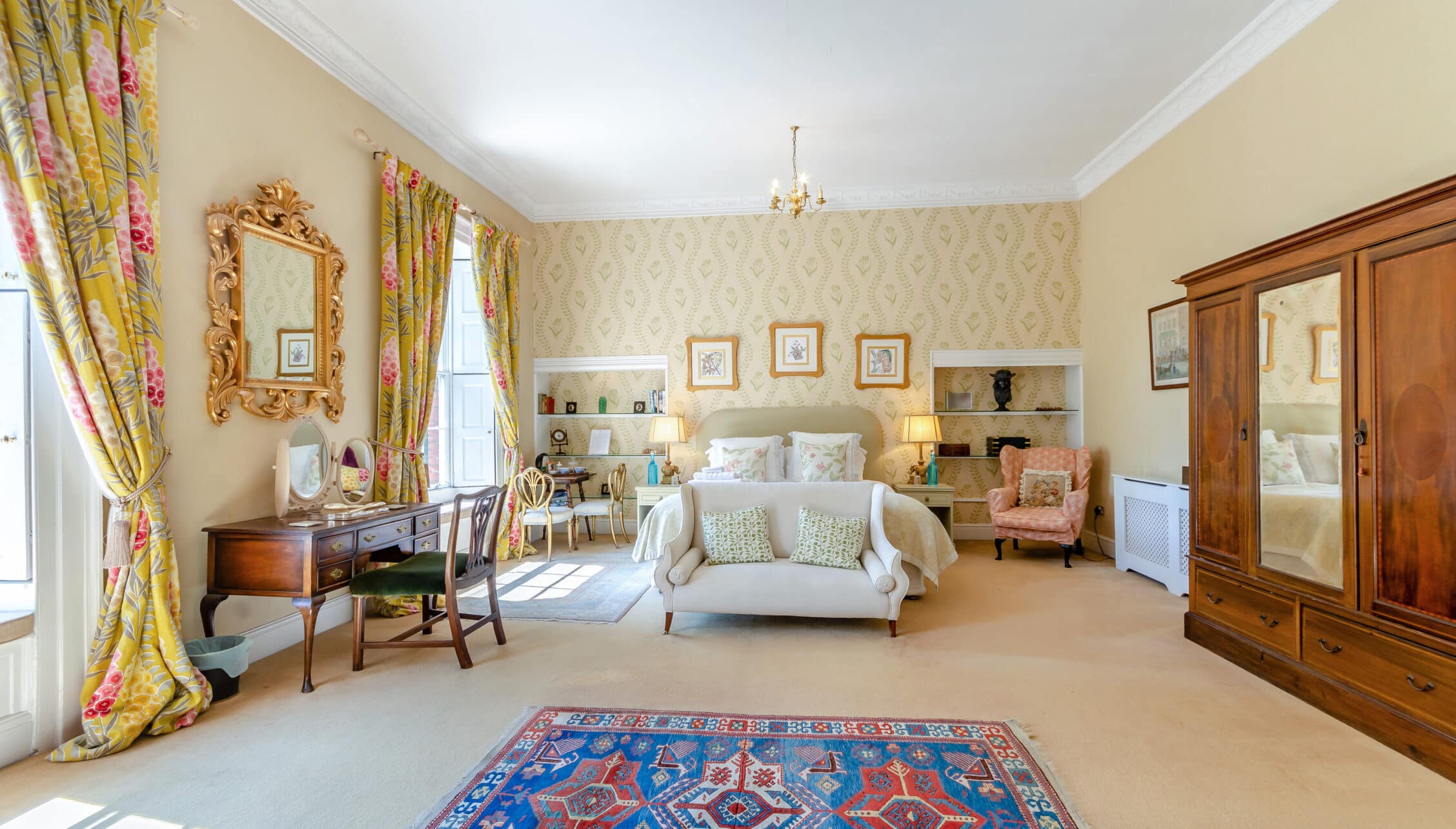 Breedon Hall, Leicestershire – Spacious bedroom with floral curtains, ornate gilt mirror, and Persian rug.