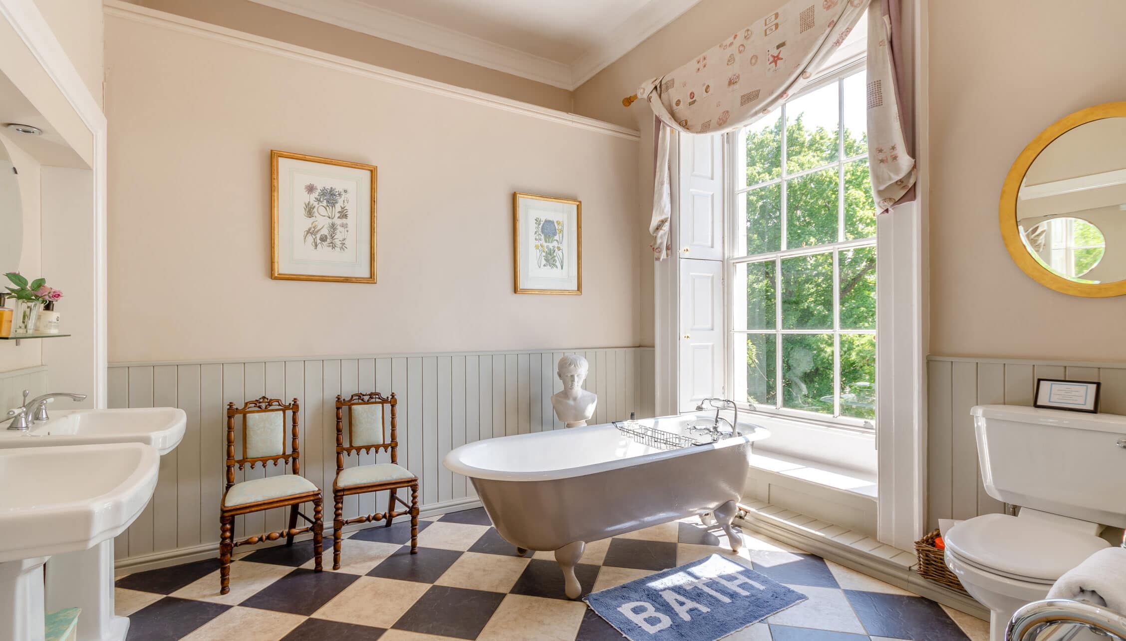 Breedon Hall, Leicestershire – Spacious bathroom with freestanding bath, panelled walls, and large sash windows overlooking grounds.