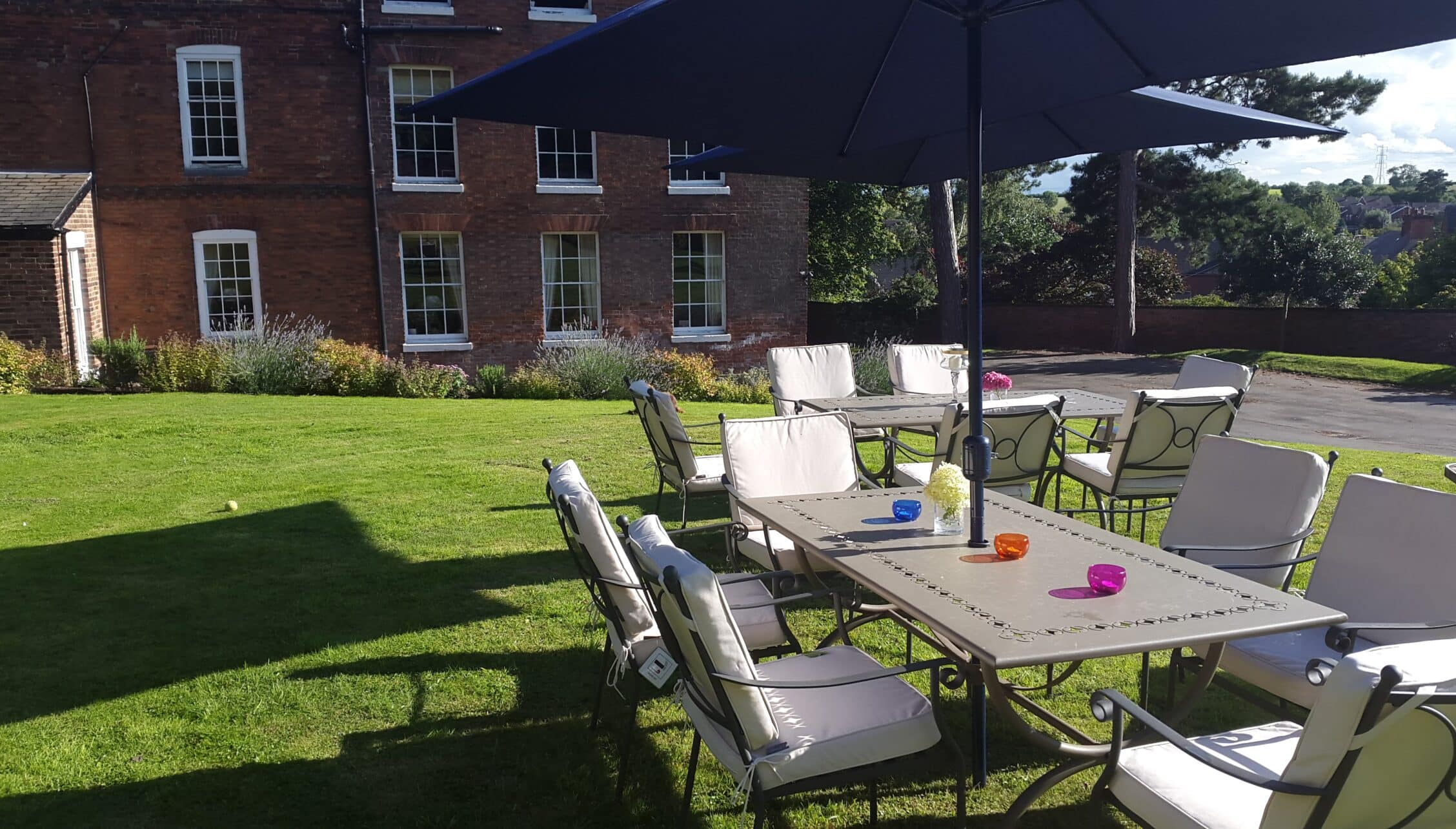 Breedon Hall, Leicestershire – Outdoor garden seating area with dining table and lounge chairs beneath black shade sail.
