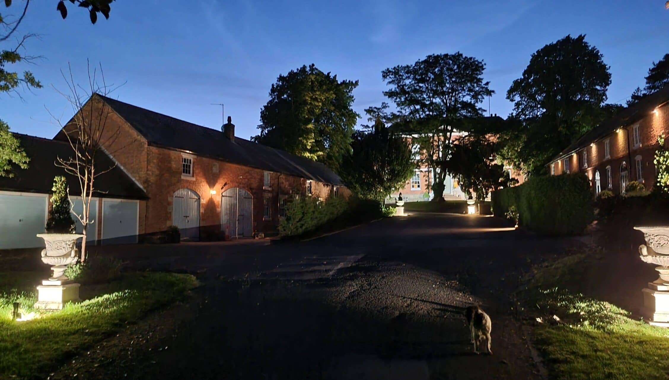 Breedon Hall, Leicestershire – Illuminated brick courtyard with converted barn buildings and mature trees at dusk.
