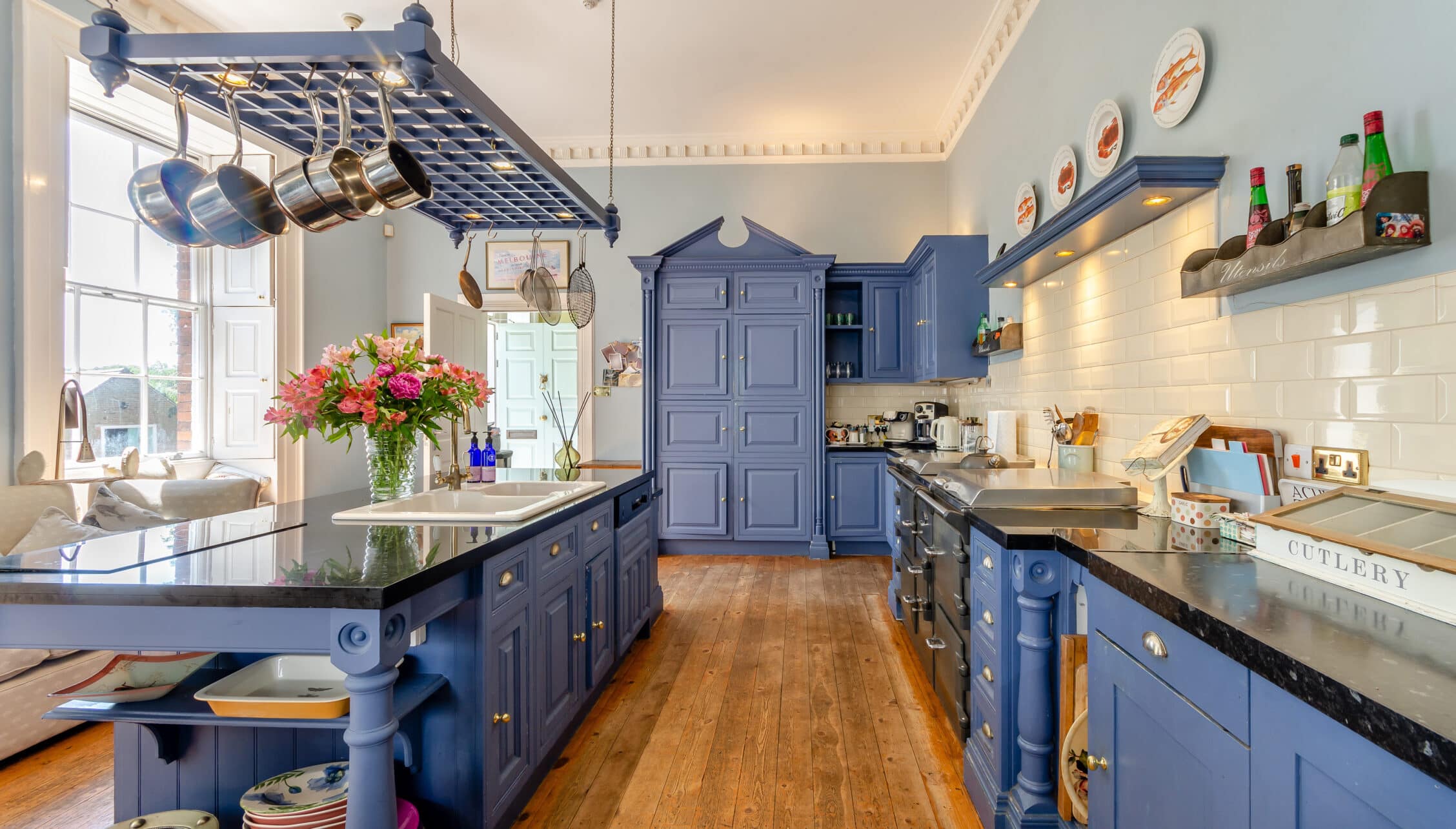 Breedon Hall, Leicestershire – Navy blue kitchen with suspended pan rack, white subway tiles, and wooden flooring.