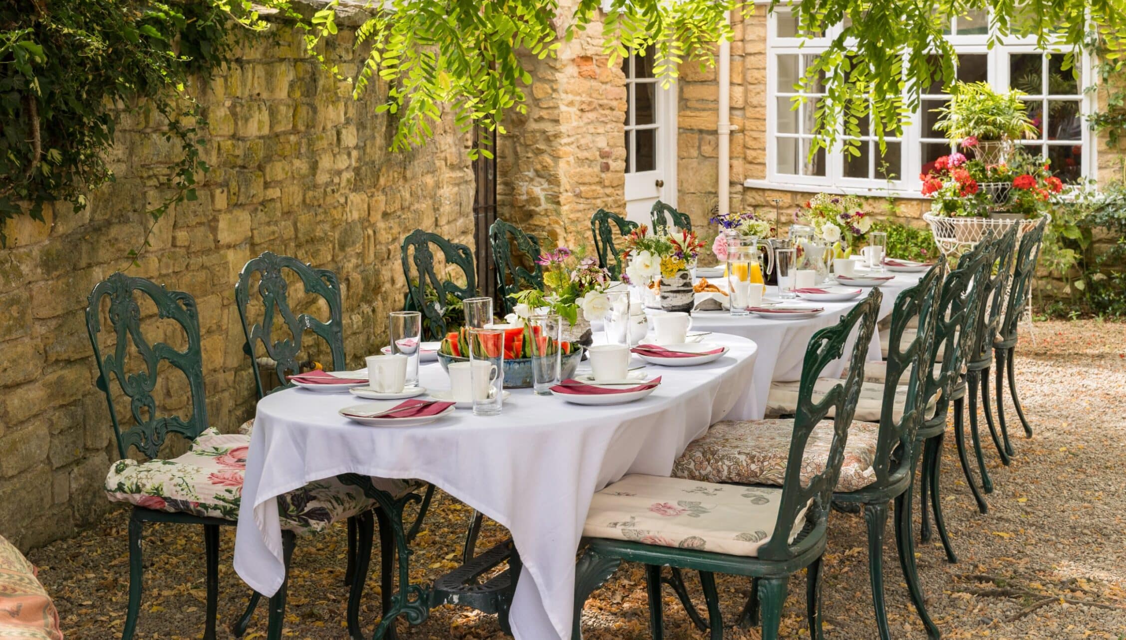 Courtyard Cottages, Gloucestershire – Outdoor courtyard dining area with stone walls, cast iron chairs, and dressed tables.