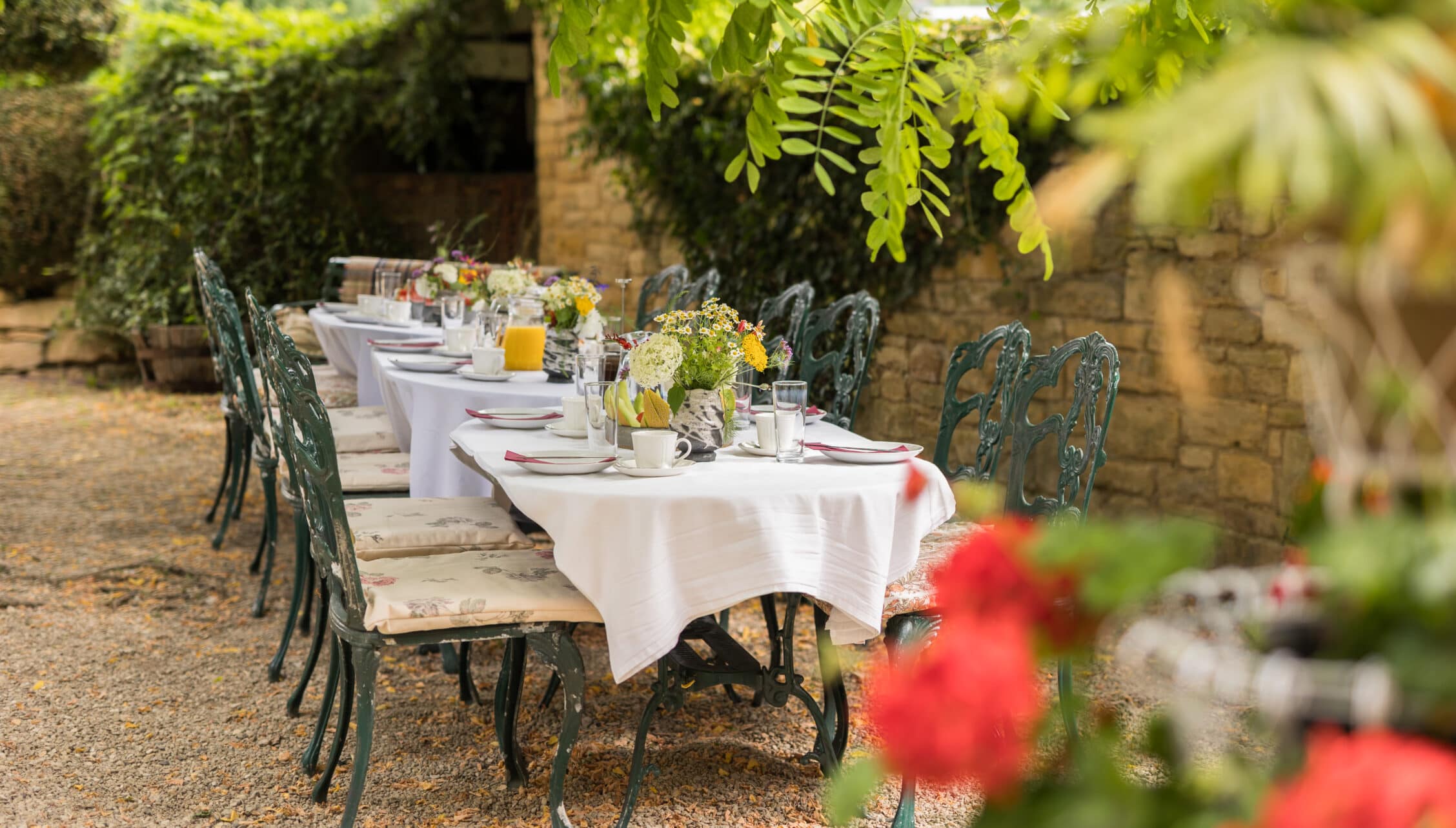 Courtyard Cottages, Gloucestershire – Outdoor dining table with white cloths and floral centrepieces in walled courtyard garden.
