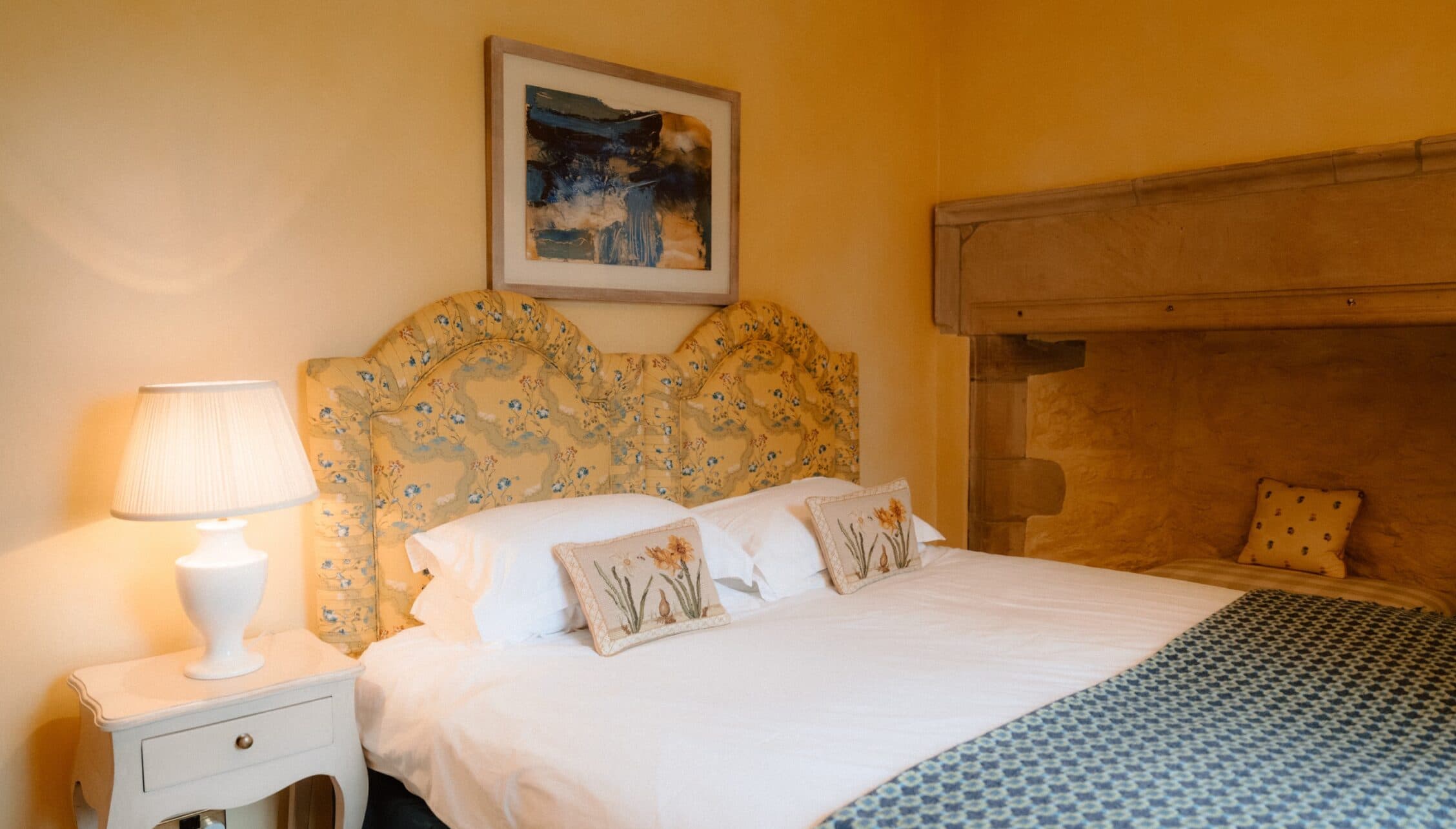 Ferniehirst Castle, East Lothian – Yellow bedroom with floral upholstered headboard and white bedside table.