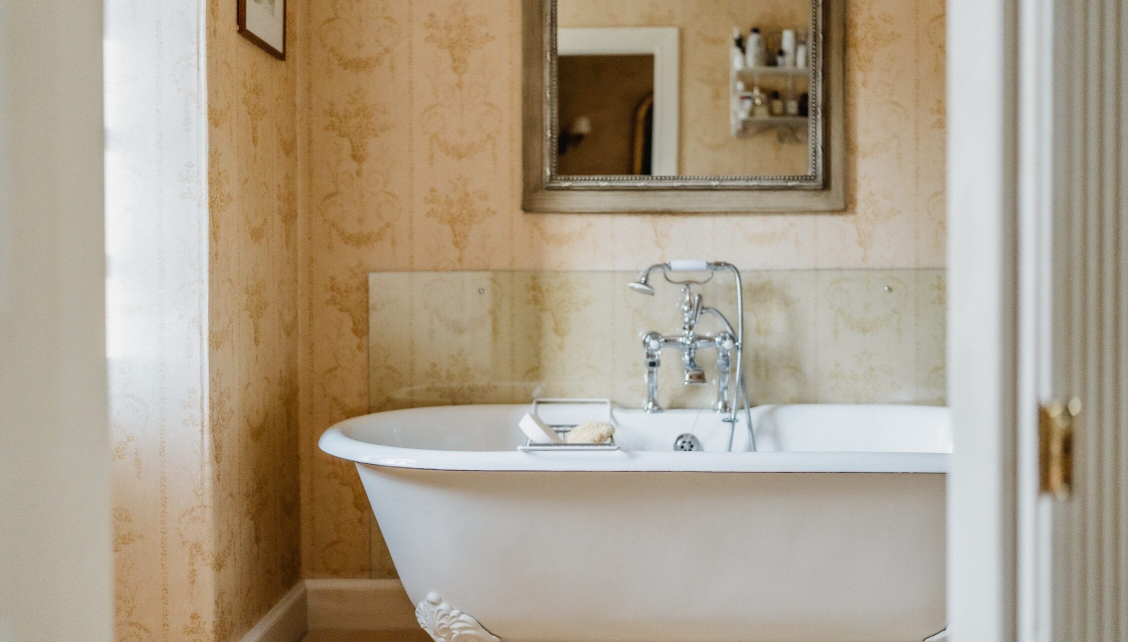 Ferniehirst Castle, East Lothian – Bathroom with freestanding white bath, traditional chrome taps and damask wallpaper.