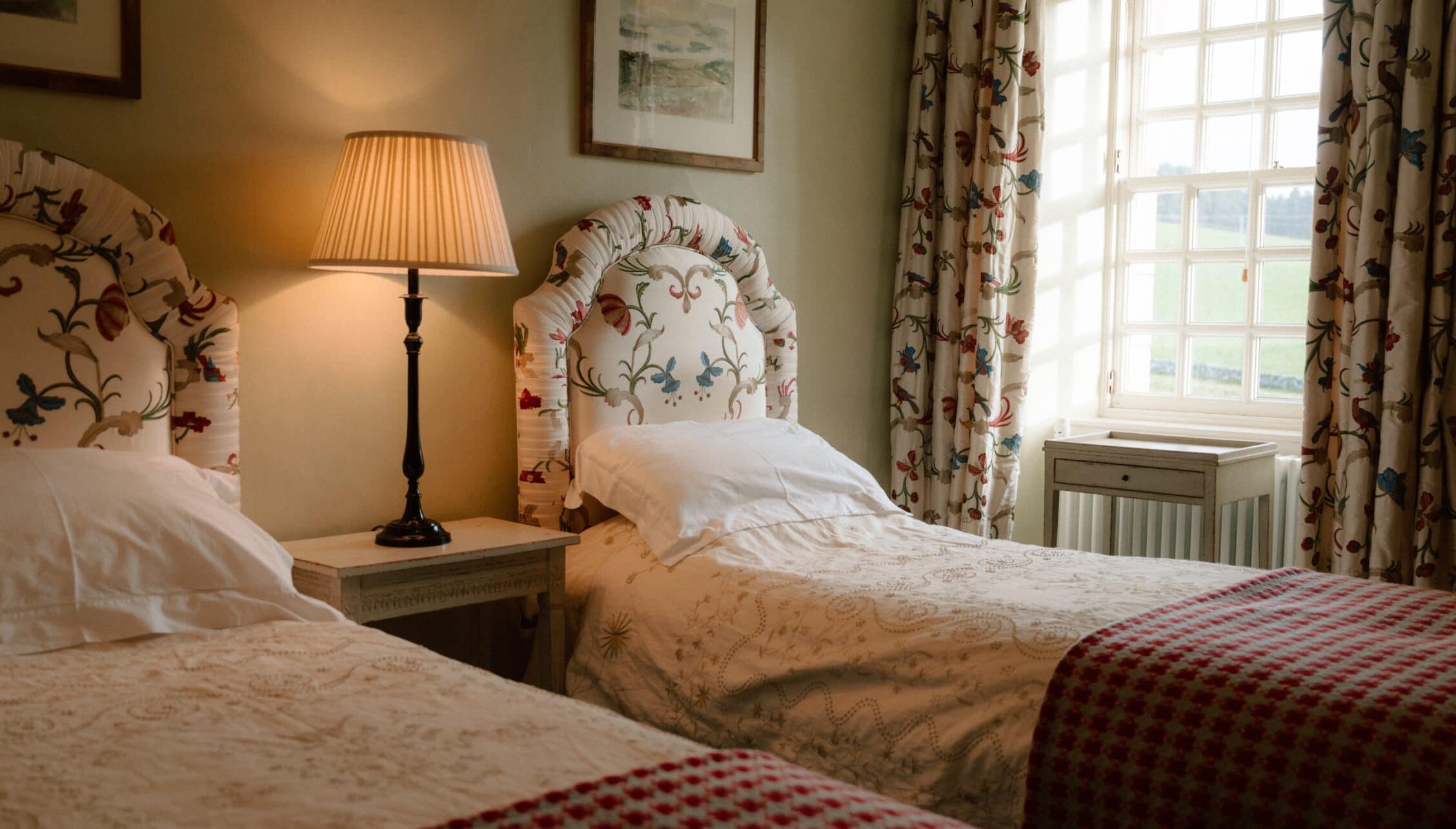 Ferniehirst Castle, East Lothian – Twin bedroom with floral headboards, table lamp and patterned curtains.
