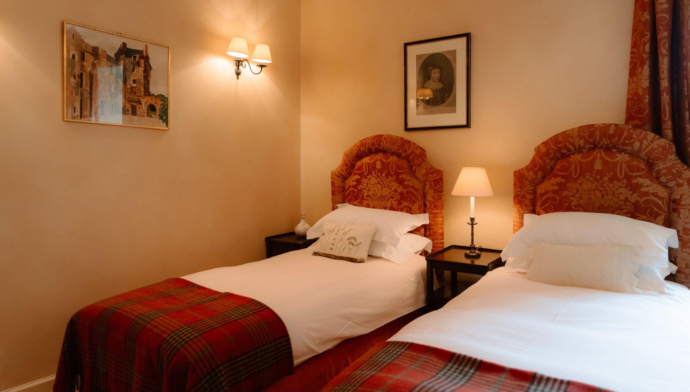 Ferniehirst Castle, East Lothian – Twin bedroom with red damask headboards and tartan throws.