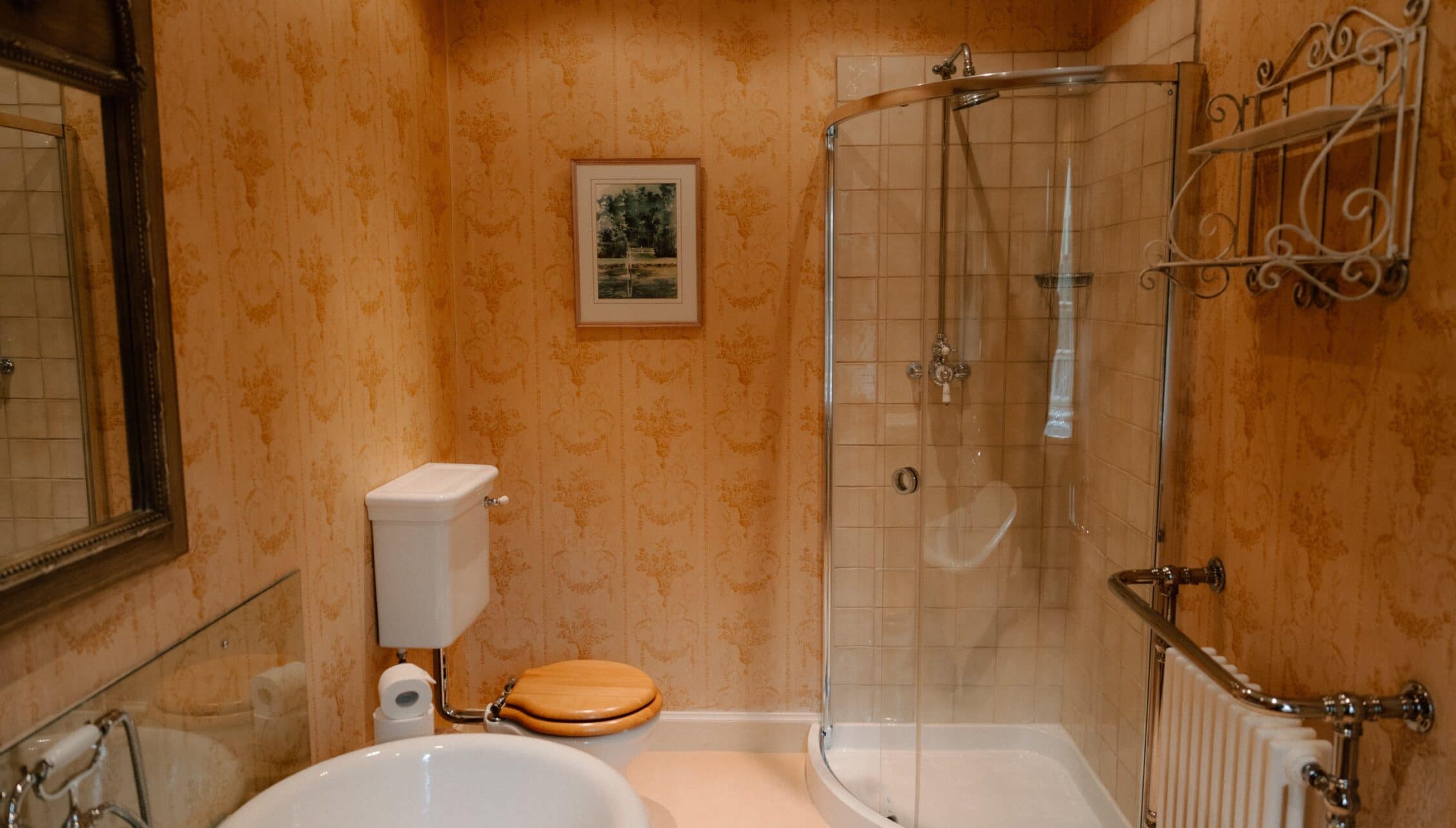 Ferniehirst Castle, East Lothian – Bathroom with apricot-patterned wallpaper, white suite, and glass shower enclosure.