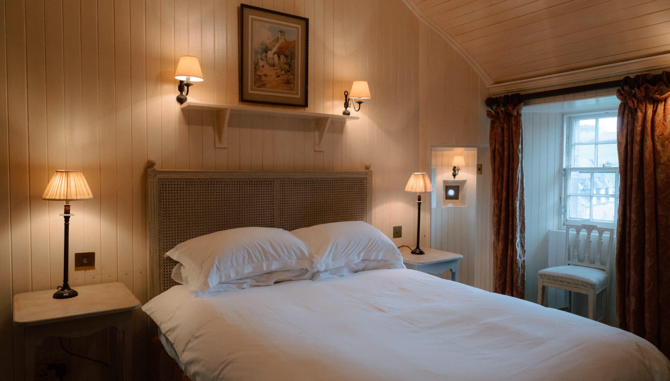 Ferniehirst Castle, East Lothian – Bedroom with wood-panelled walls, double bed with wicker headboard, and bedside lamps.
