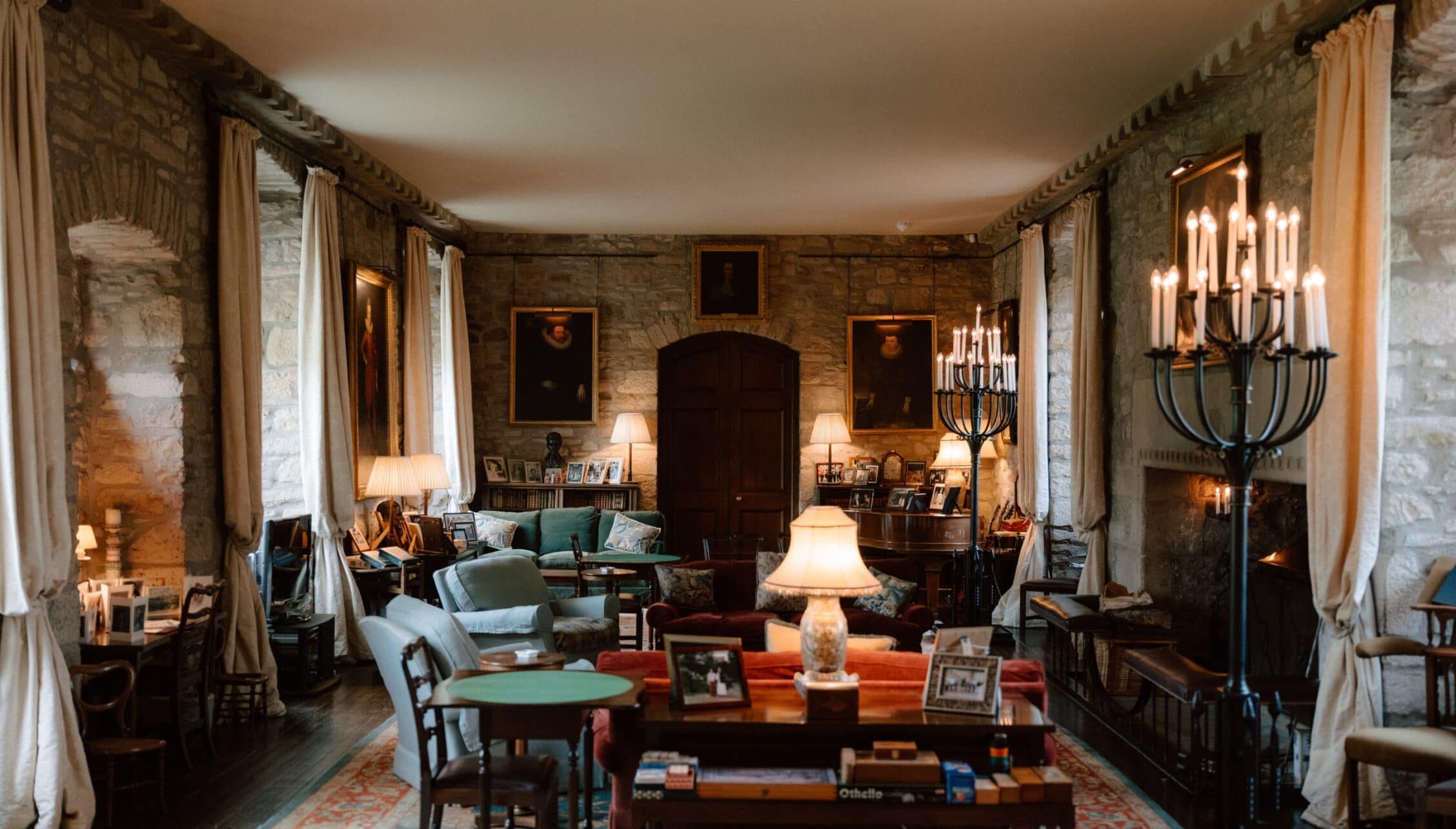 Ferniehirst Castle, East Lothian – Grand stone hall with arched doorway, candelabra lighting, and upholstered seating.