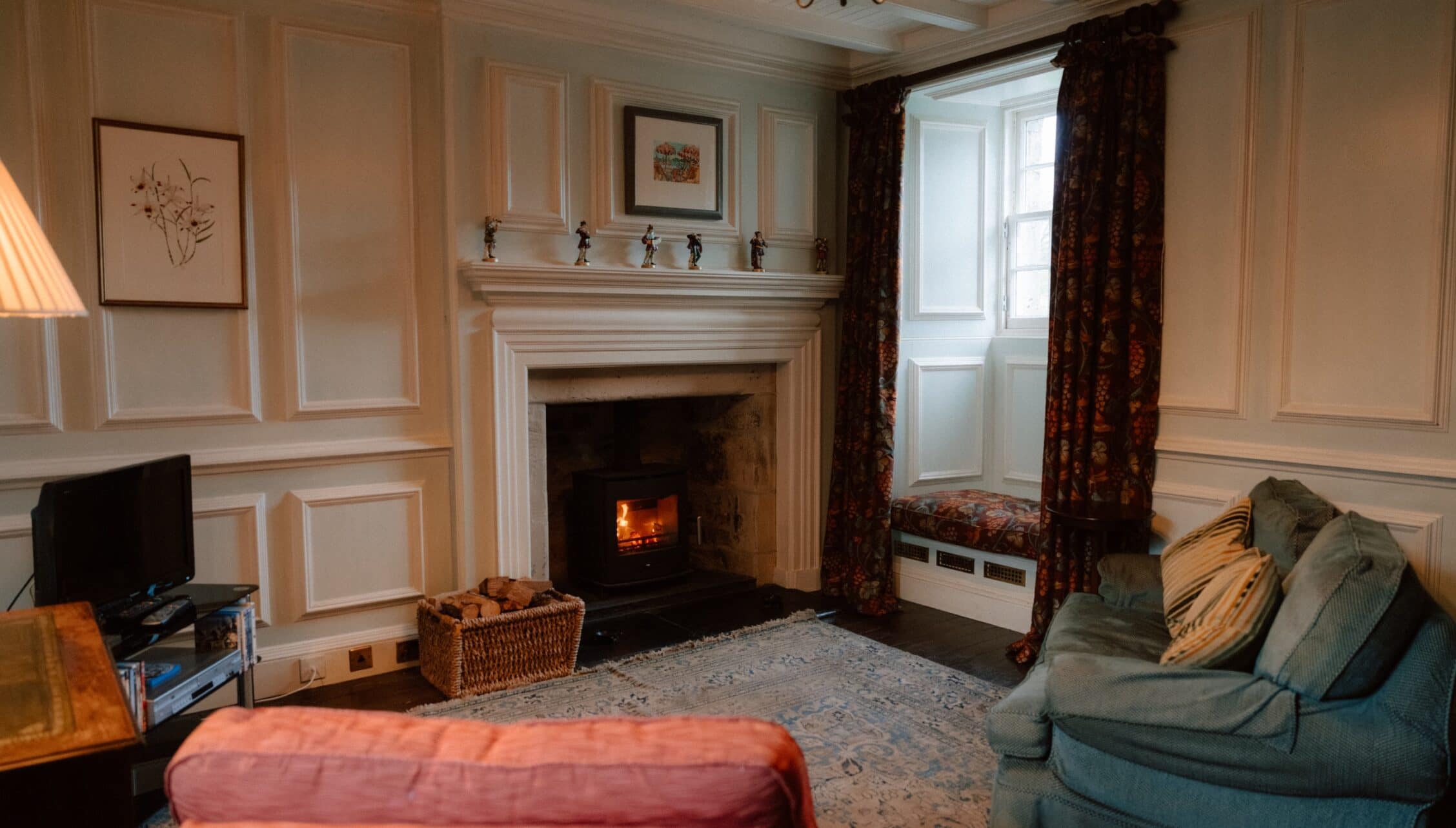 Ferniehirst Castle, East Lothian – Classic sitting room with cream panelled walls, wood-burning stove and upholstered seating.