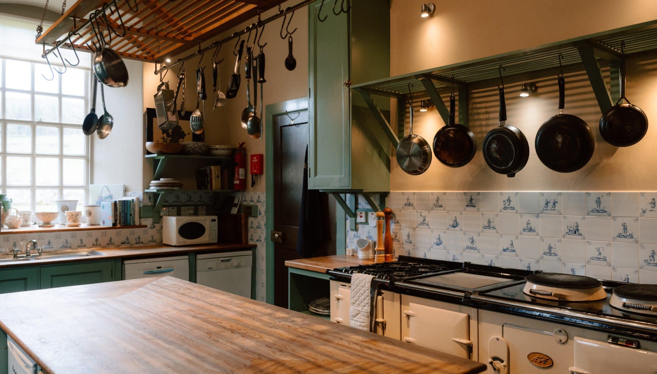 Ferniehirst Castle, East Lothian – Kitchen with green cabinetry, gas range, and hanging cast-iron cookware.