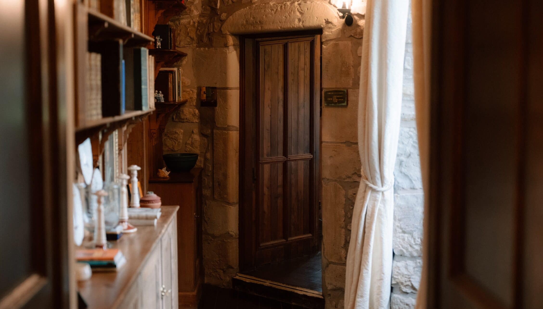 Ferniehirst Castle, East Lothian – Narrow stone corridor with wooden door and wall-mounted shelving.