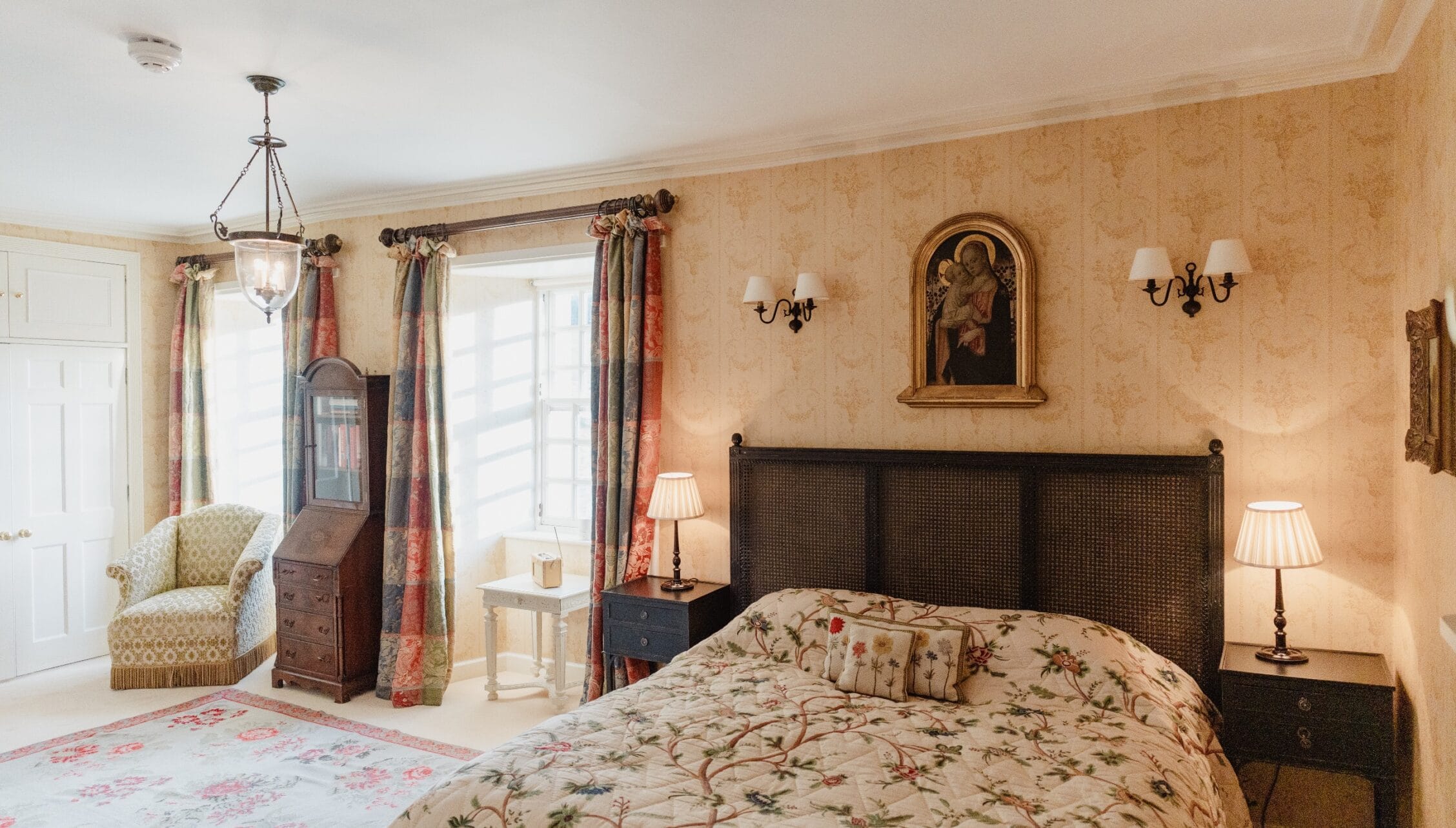 Ferniehirst Castle, East Lothian – Bedroom with peach damask wallpaper, dark wood bed with rattan headboard, and patterned curtains.