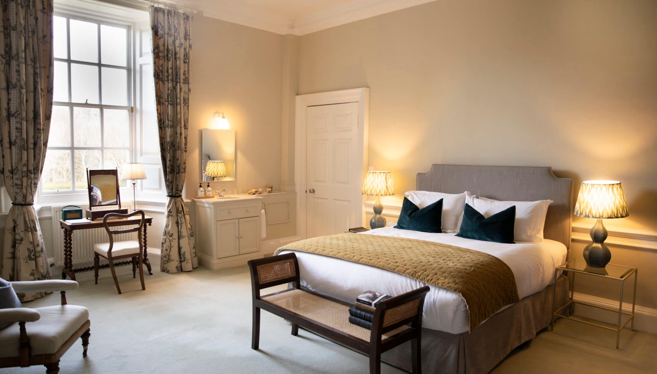 Gilmerton House, East Lothian – Spacious bedroom with grey upholstered bed, twin bedside lamps and period dressing table.