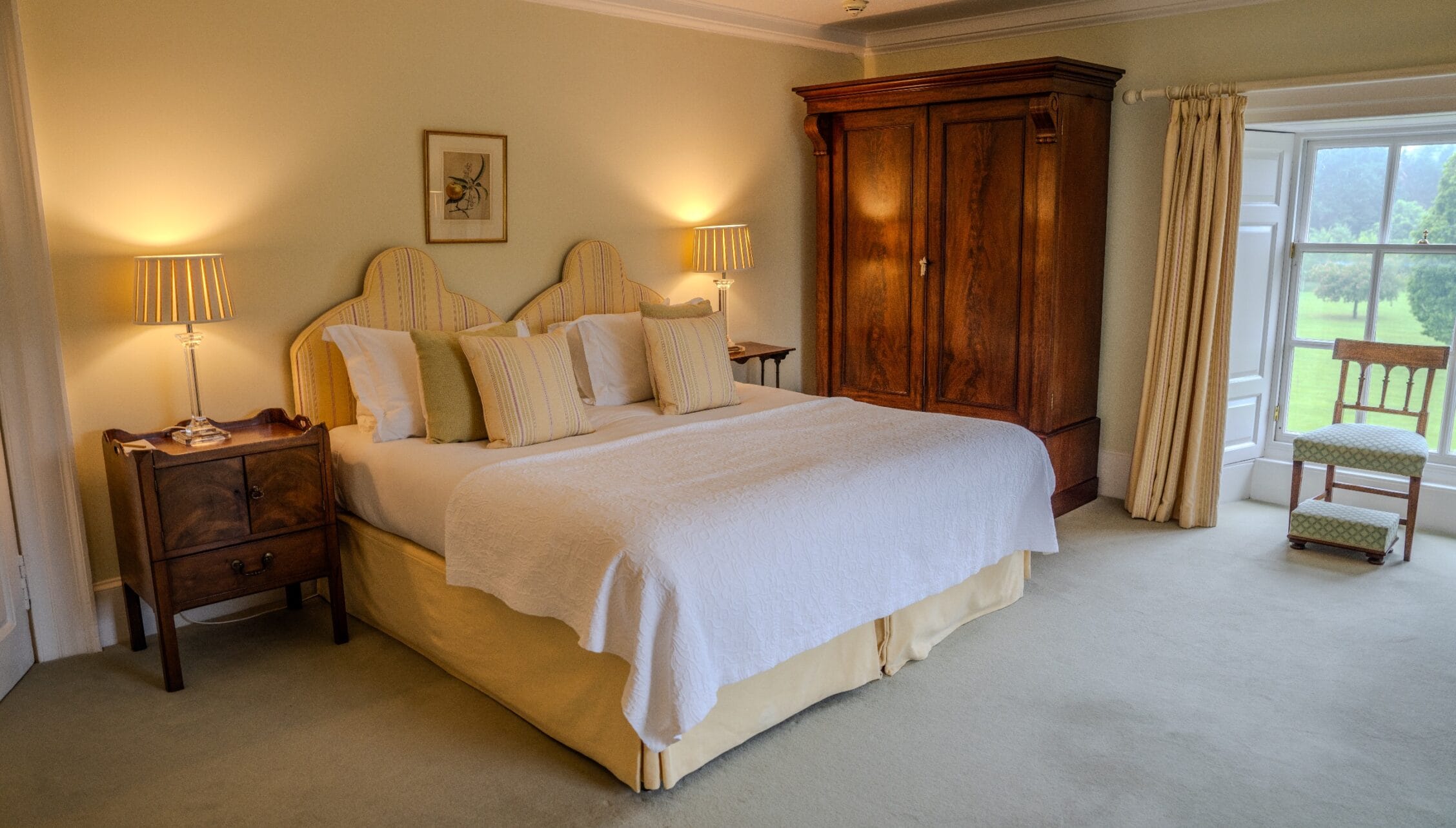 Gilmerton House, East Lothian – Spacious bedroom with upholstered bed, wooden wardrobe and countryside views through large windows.