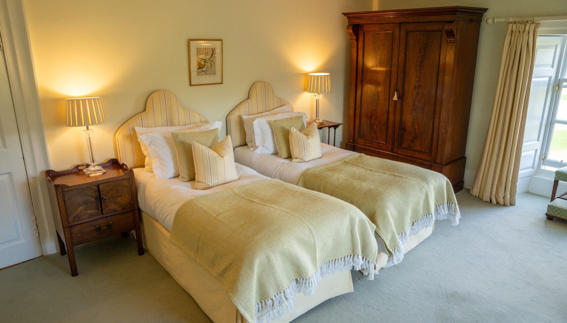 Gilmerton House, East Lothian – Twin beds with striped headboards and cream wool throws in bedroom with wooden wardrobe.