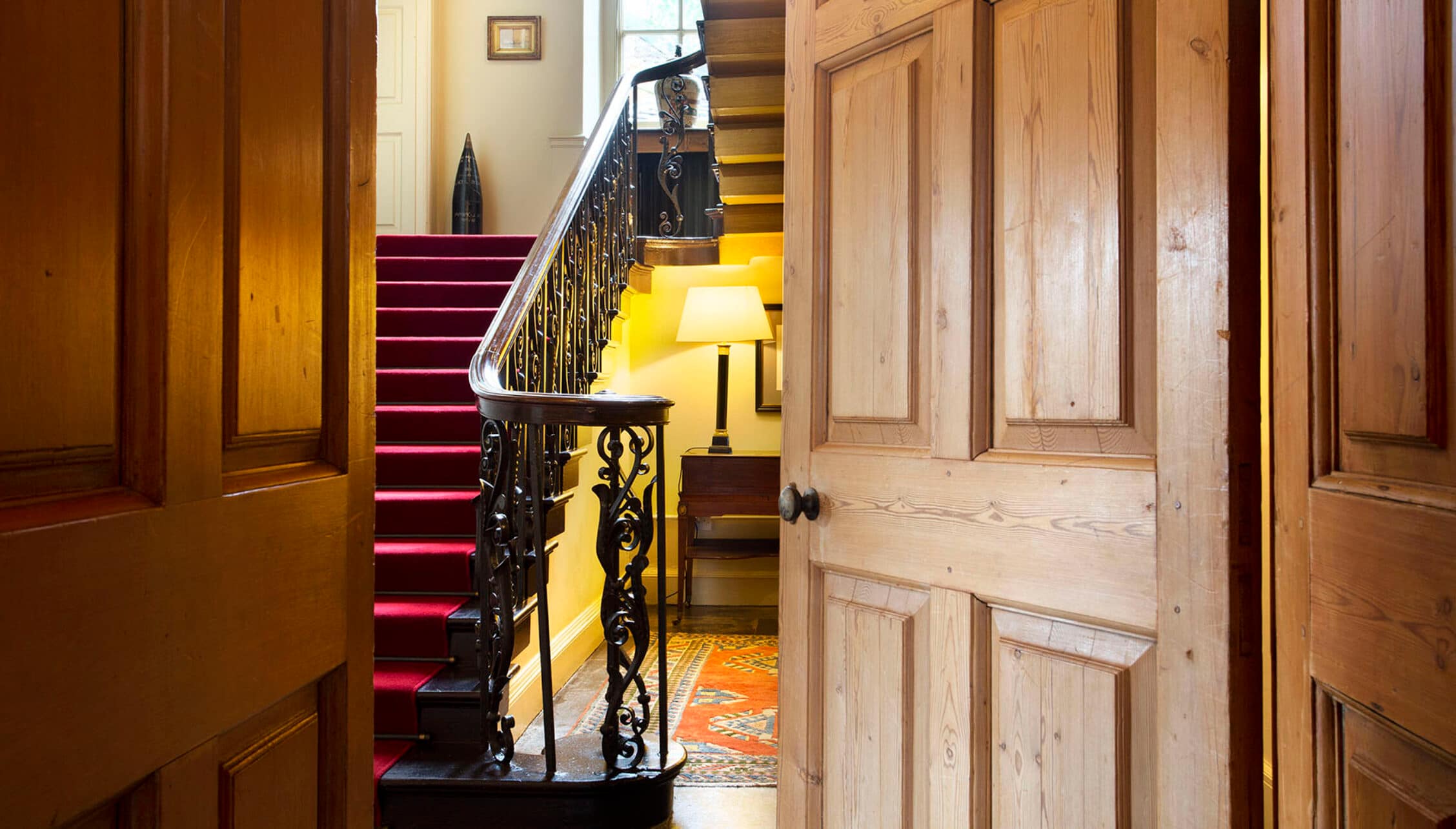 Gilmerton House, East Lothian – Grand hallway with burgundy staircase, ornamental iron railings and wooden doors.